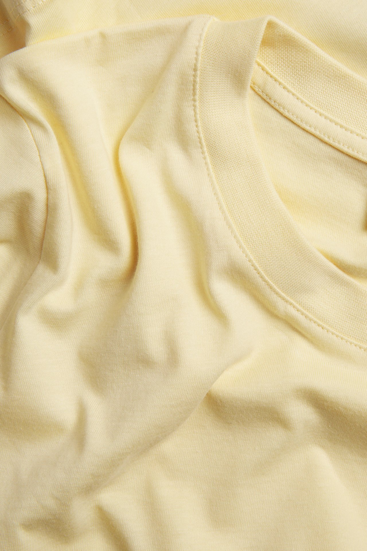 Zbliżenie na jasnożółty bawełniany T-shirt o prostym kroju, widoczna struktura tkaniny i szwy.