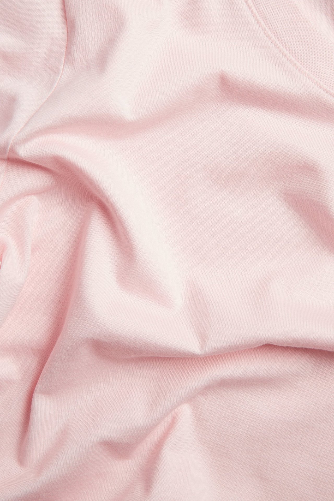 Nærbilde av lyserosa, ensfarget bomulls-T-skjortestoff med myke folder.