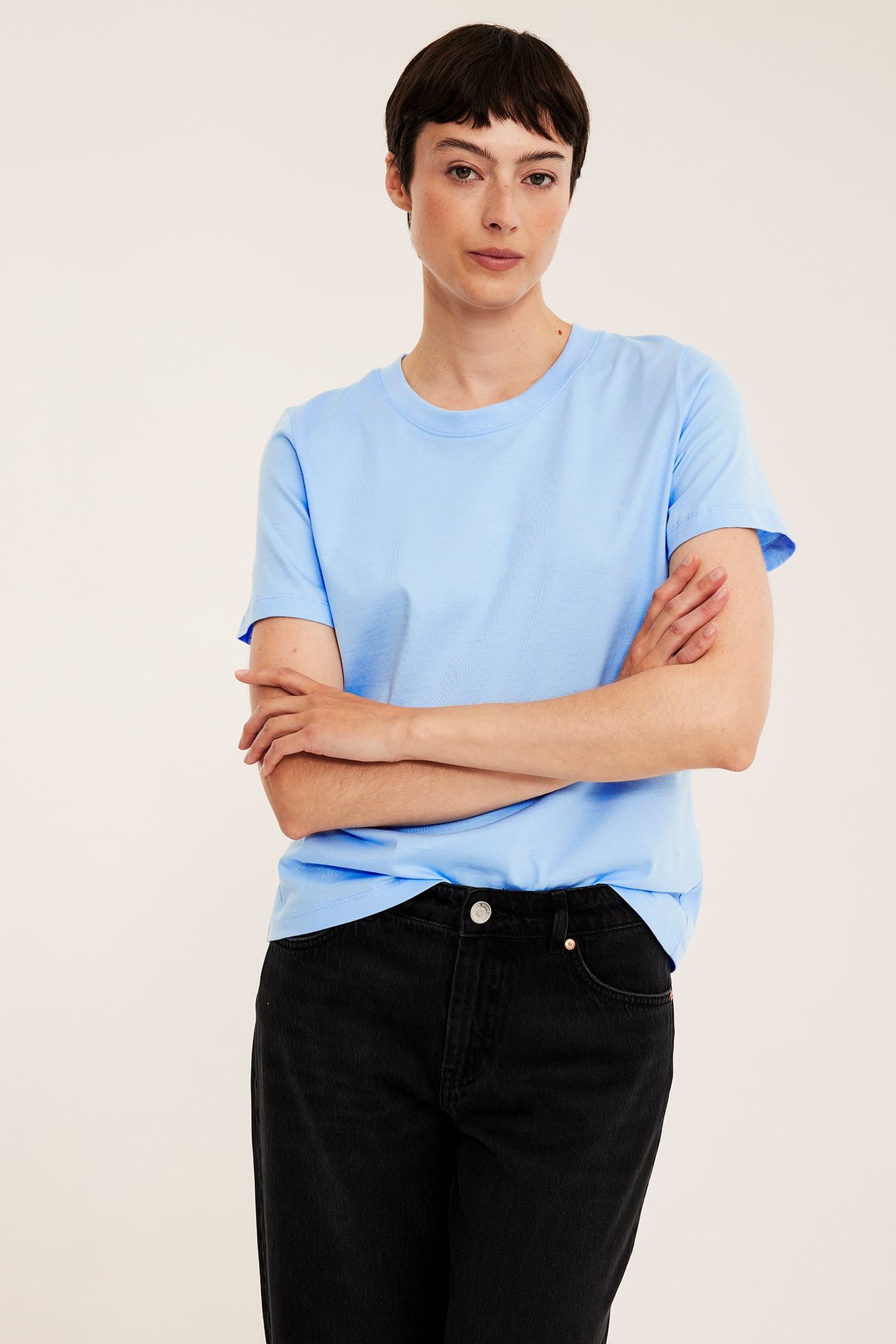 Forfra: kvinne i lyseblå regular fit bomulls t-skjorte og svarte jeans.
