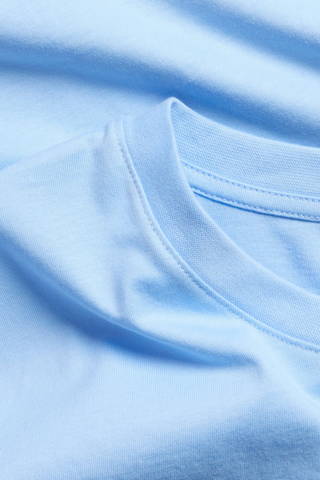 Närbild på en ljusblå, enfärgad T-shirt i bomull med rak passform och rund halsringning.