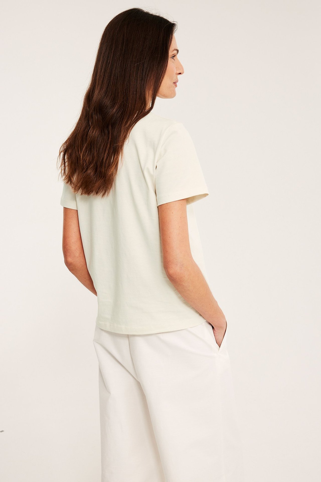 Naisen sivukuva yllään luonnonvalkoinen suoraleikattu puuvillainen T-paita ja valkoiset housut.