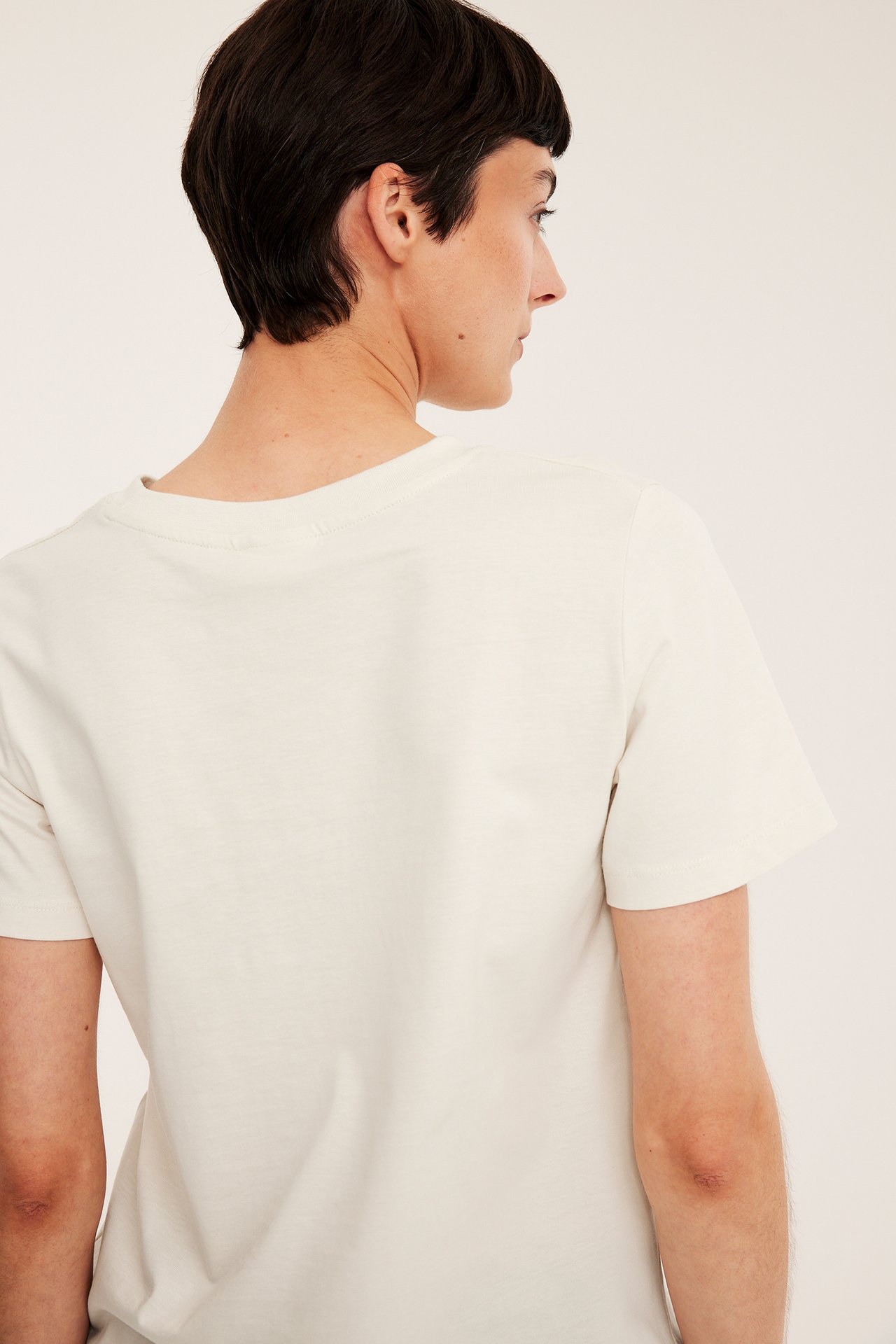 Rygg-/sidovy av en kvinna i en enfärgad offwhite t-shirt i bomull med rak passform.