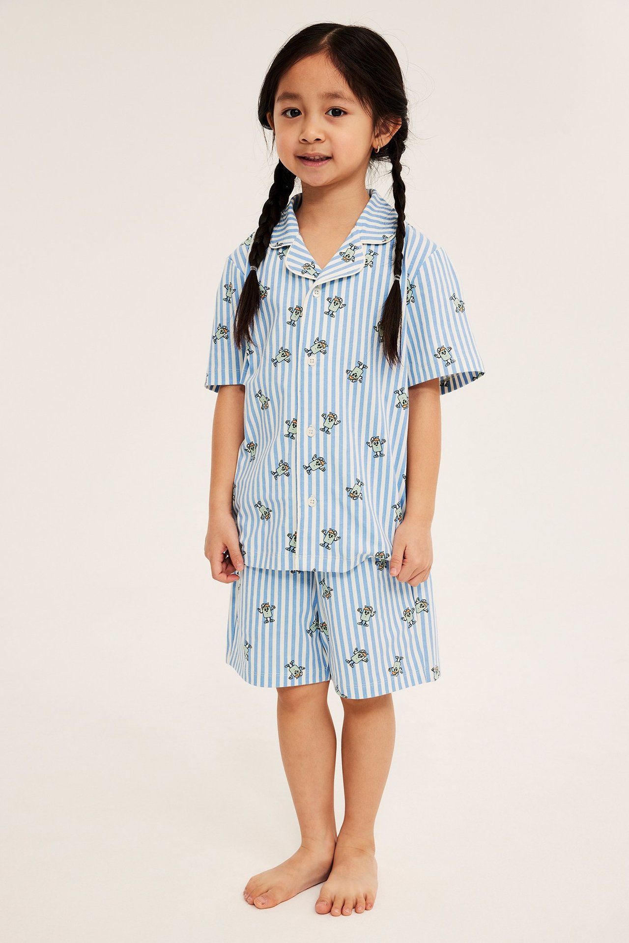 Edestä: Lapsi yllään vaaleansininen ja valkoraidallinen pyjamassetti hirviökuviolla.