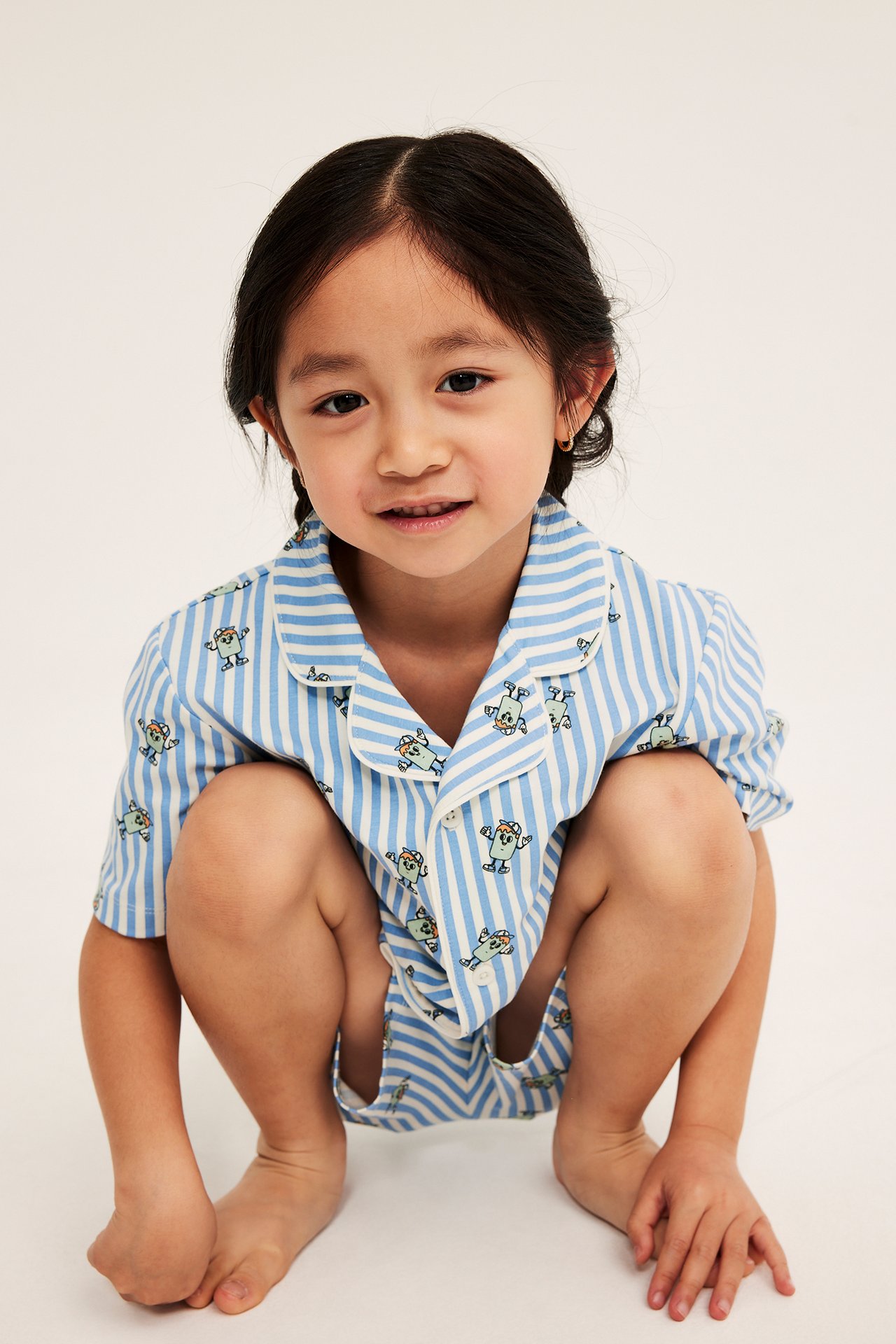 Från framsidan: Ett barn i ett ljusblått och vitrandigt kort pyjamasset med karaktärstryck.