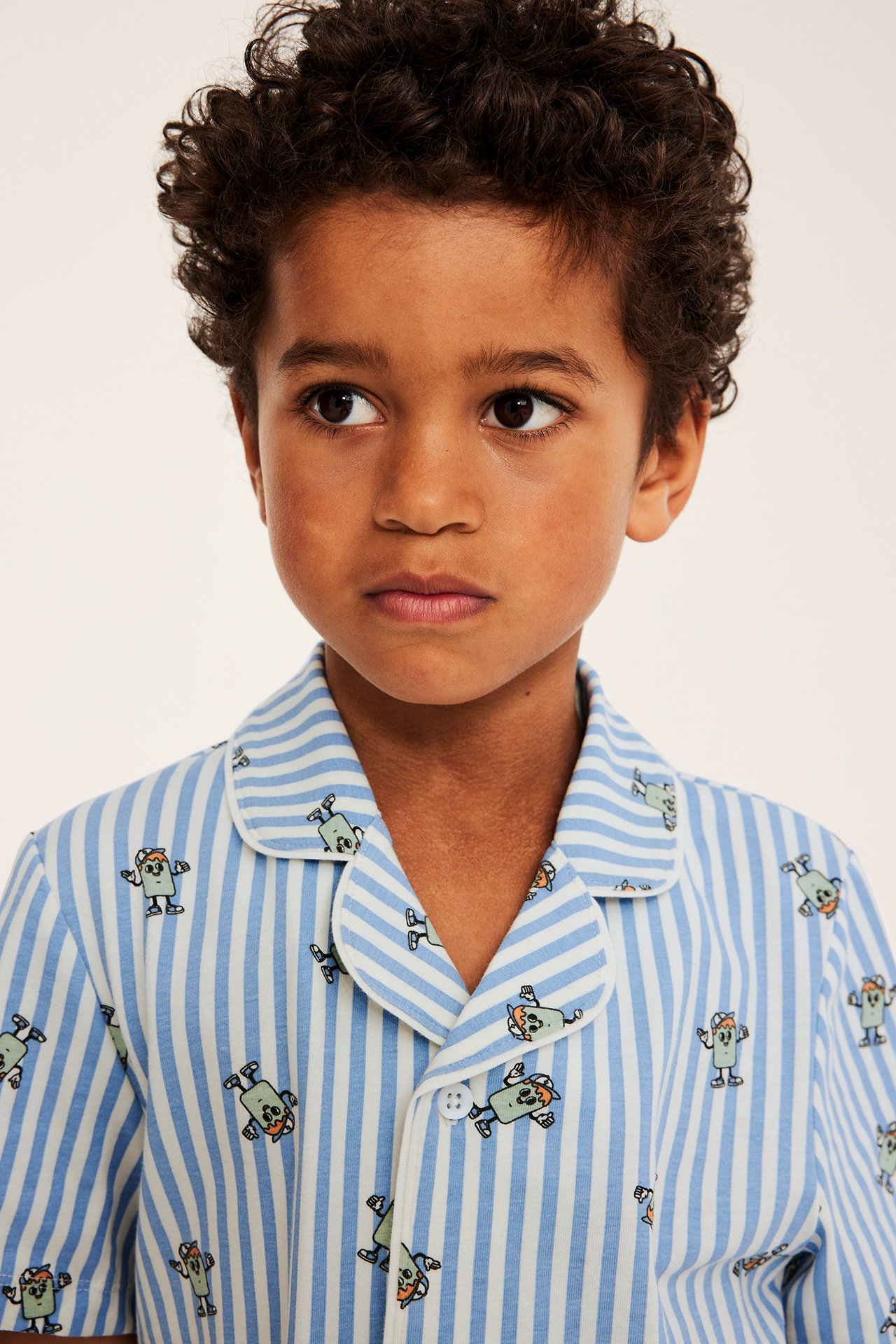 Lähikuva lapsesta, jolla on kauluksellinen, vaaleansinivalkoraidallinen pyjamatoppi hahmopainatuksella.