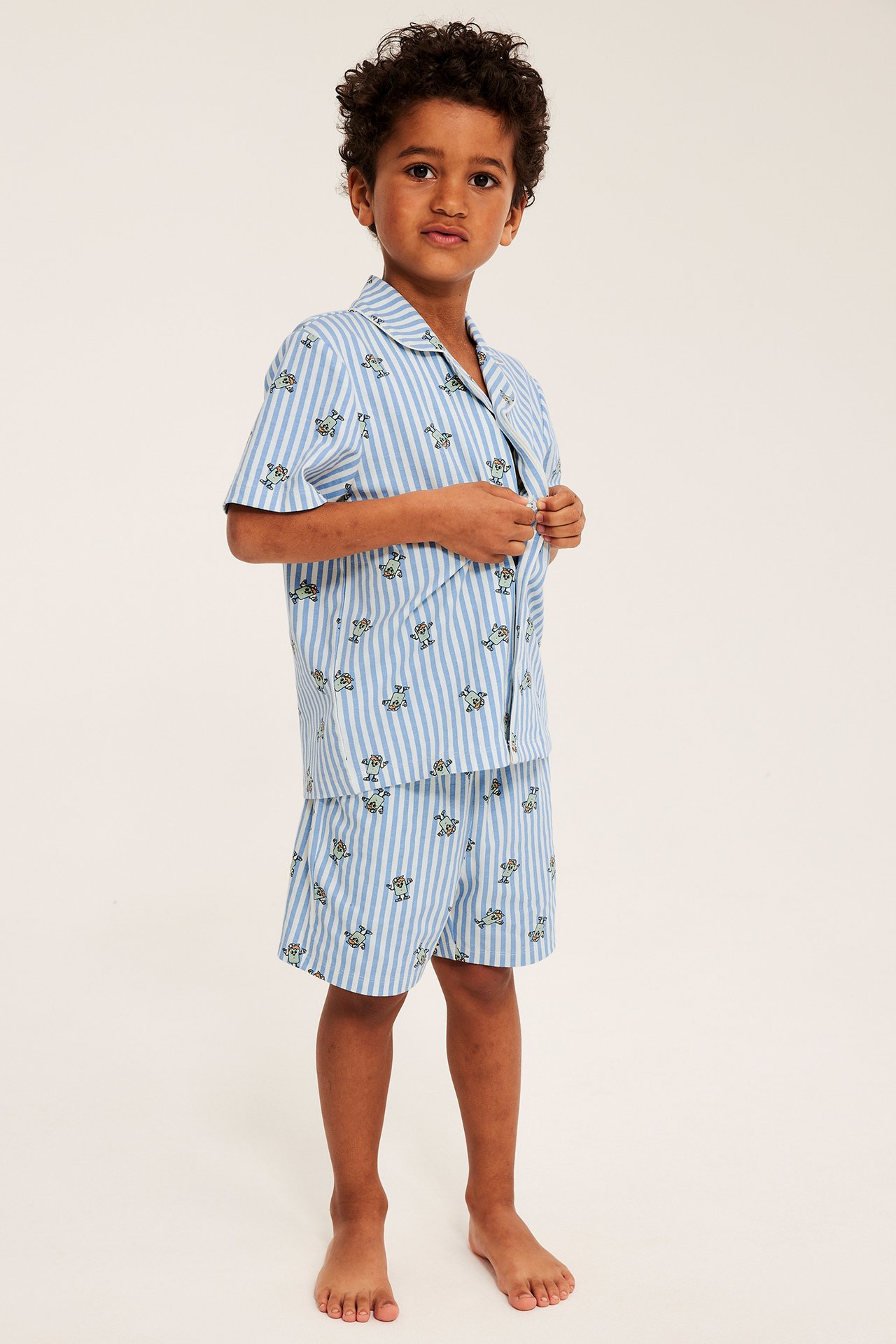 Edestä kuvattu lapsi vaaleansinivalkoisessa raidallisessa lyhyessä pyjamasssetissä, jossa hahmopainatus.