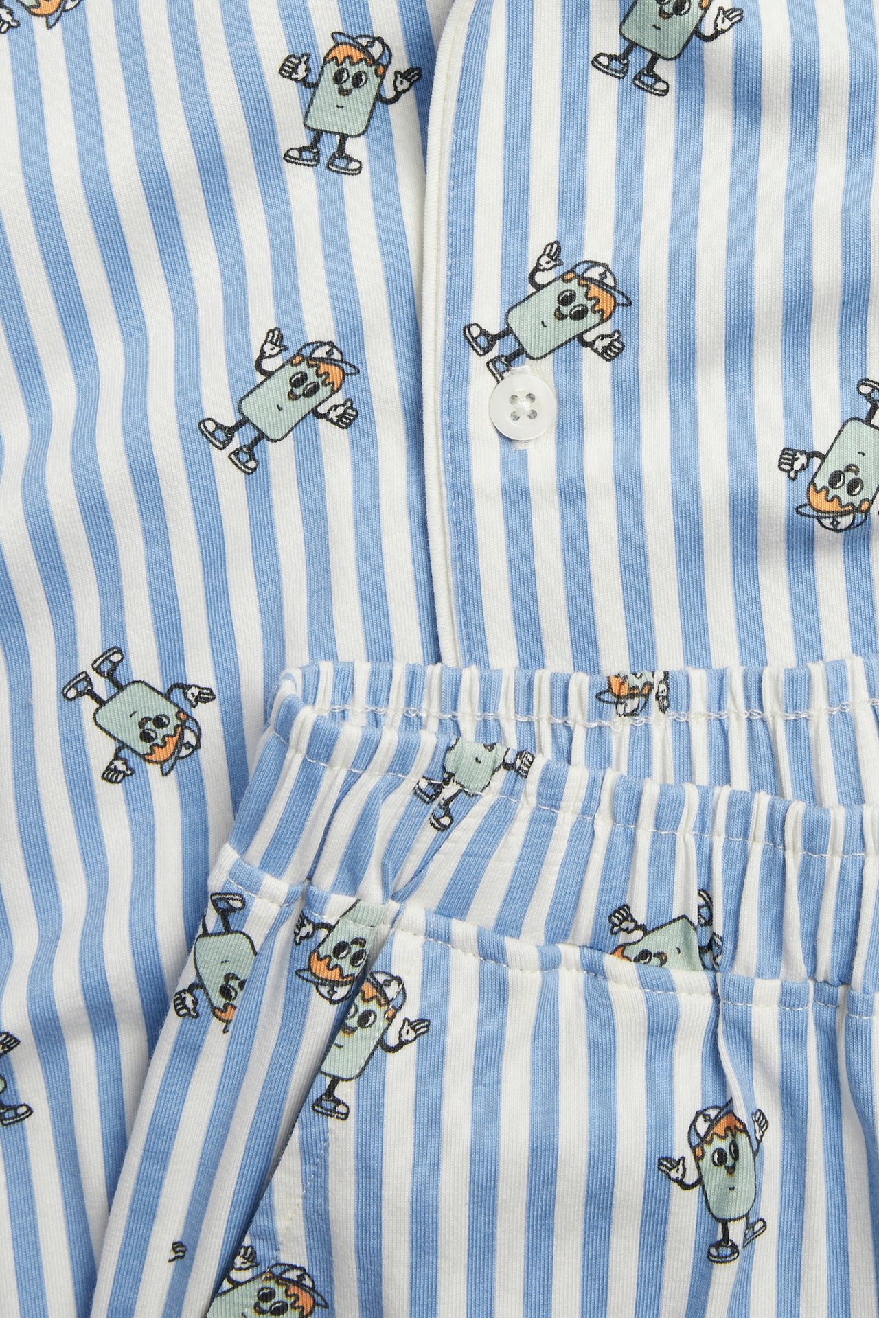 Närbild: randigt barnpyjamasset i vitt och blått med figurtryck, knappad topp och resårshorts.