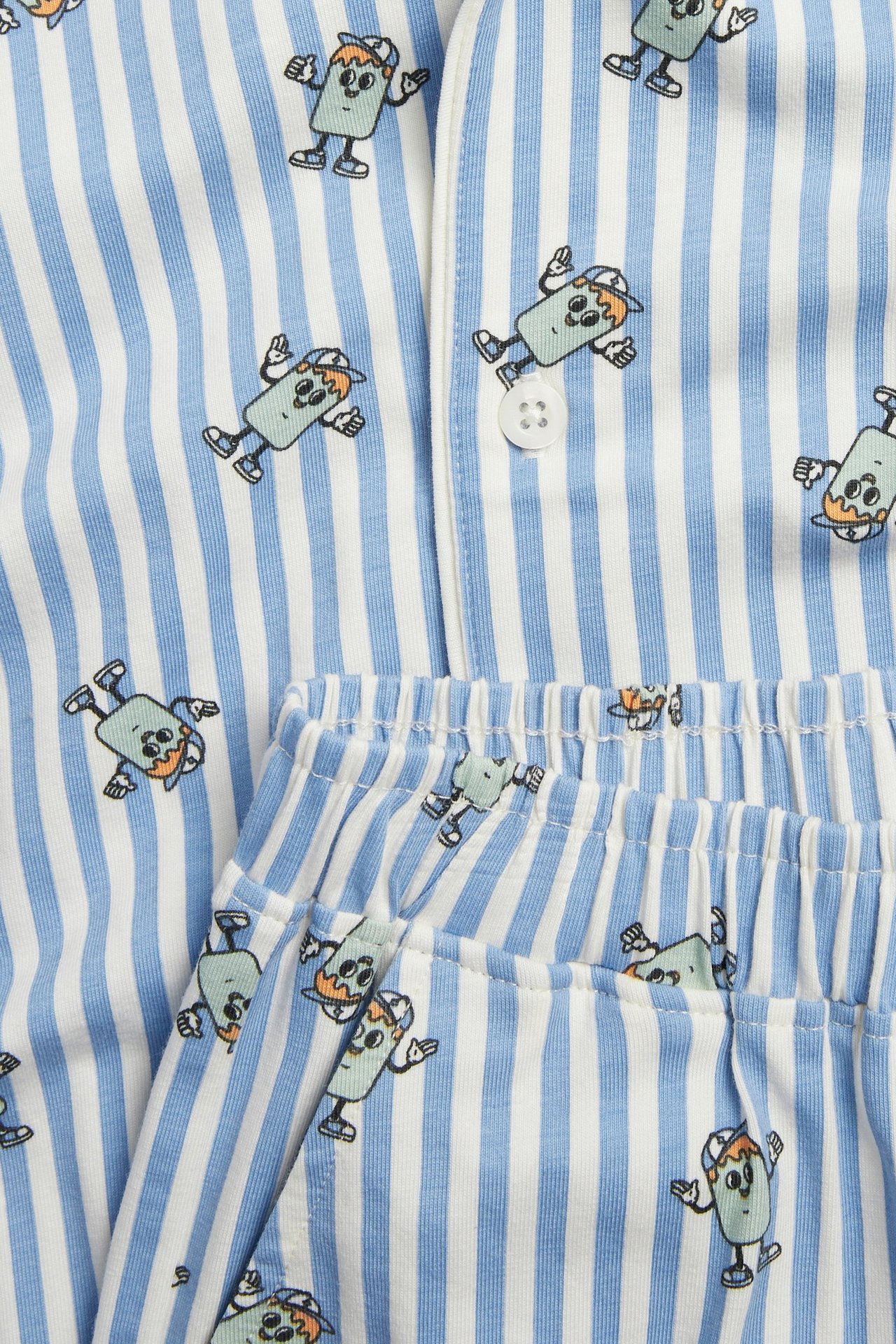 Zbliżenie: biało-niebieska piżama dziecięca w paski z nadrukiem postaci, zapinana góra, spodenki na gumce.