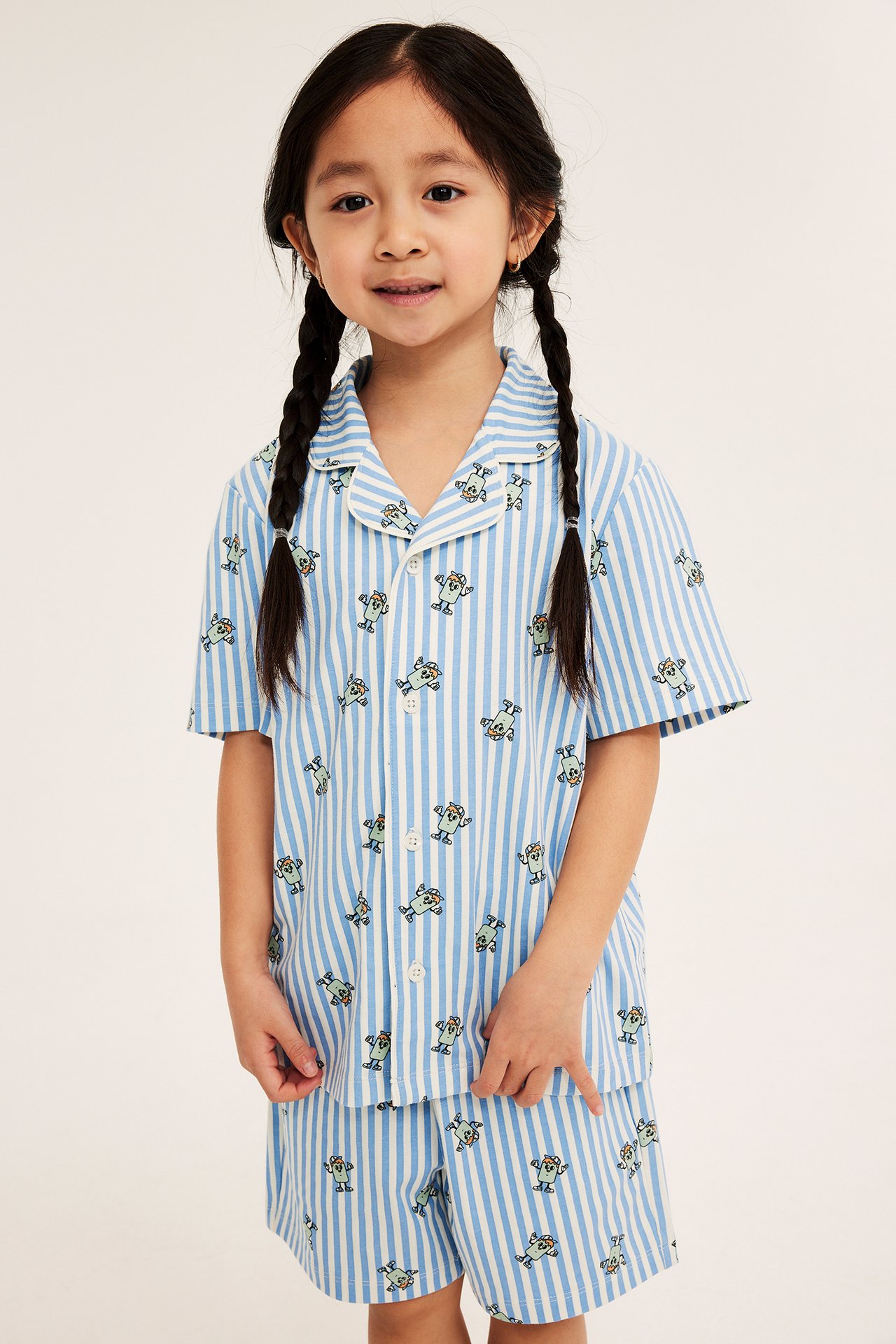 Framifrån, ett barn i en blå- och vitrandig pyjamas i bomull med korta ärmar och monsterprint.