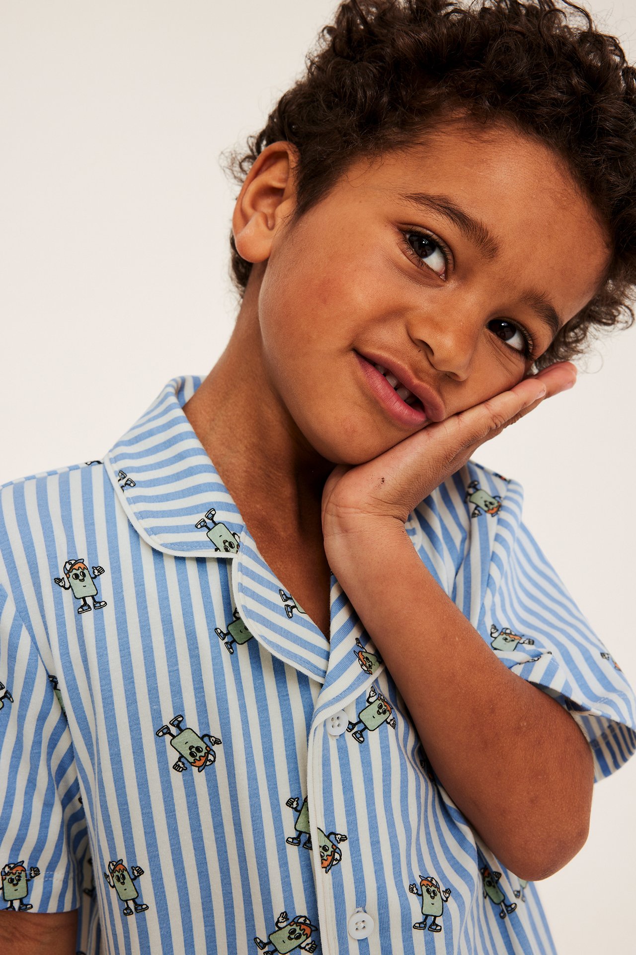 Lähikuva hymyilevästä lapsesta, jolla on luonnonvalkoinen ja siniraitainen lyhythihainen pyjaman yläosa hahmokuvioinnilla.