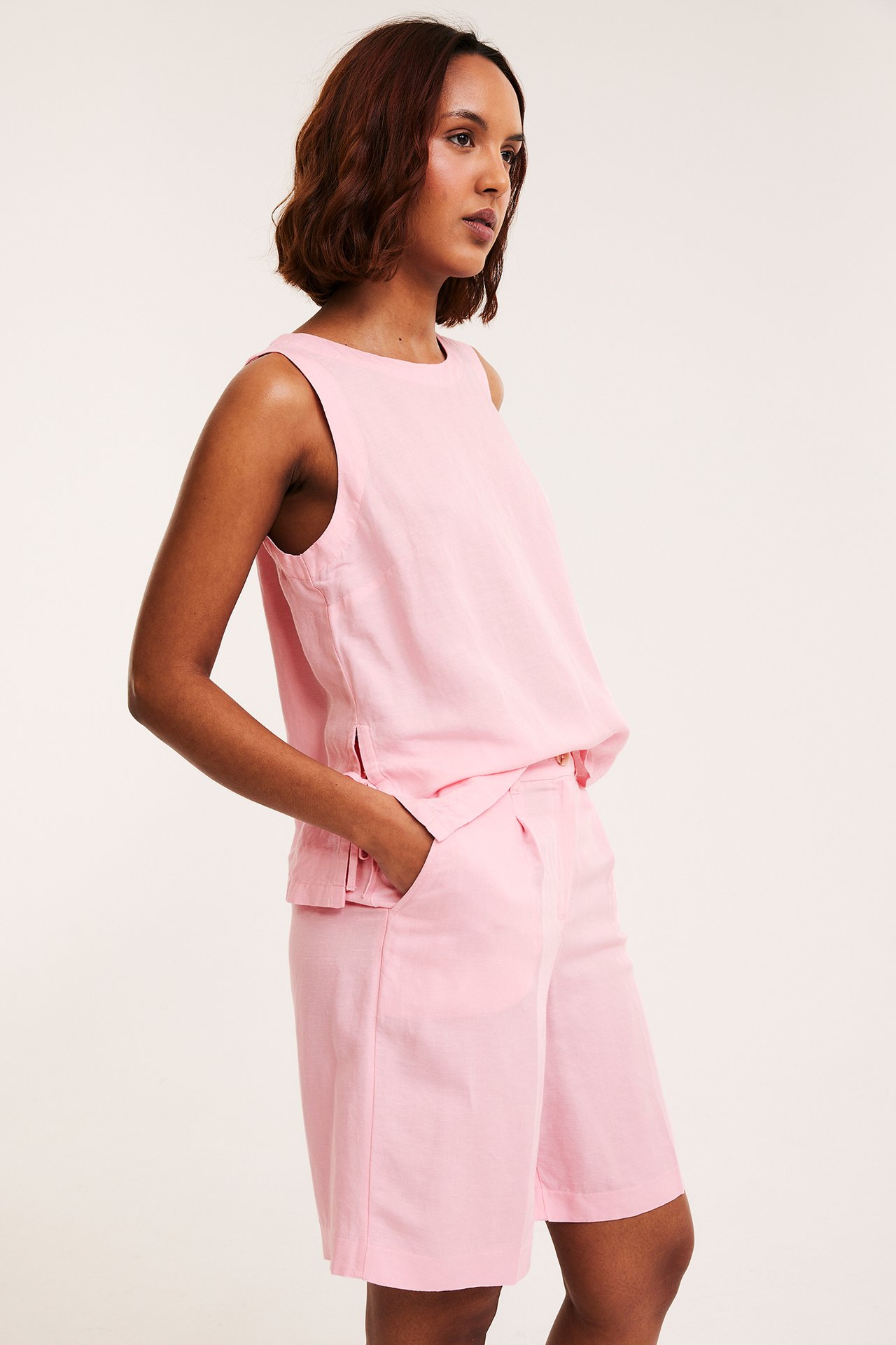Sidebilde av kvinne i rosa dressede shorts i linblanding med folder og matchende ermeløs topp.