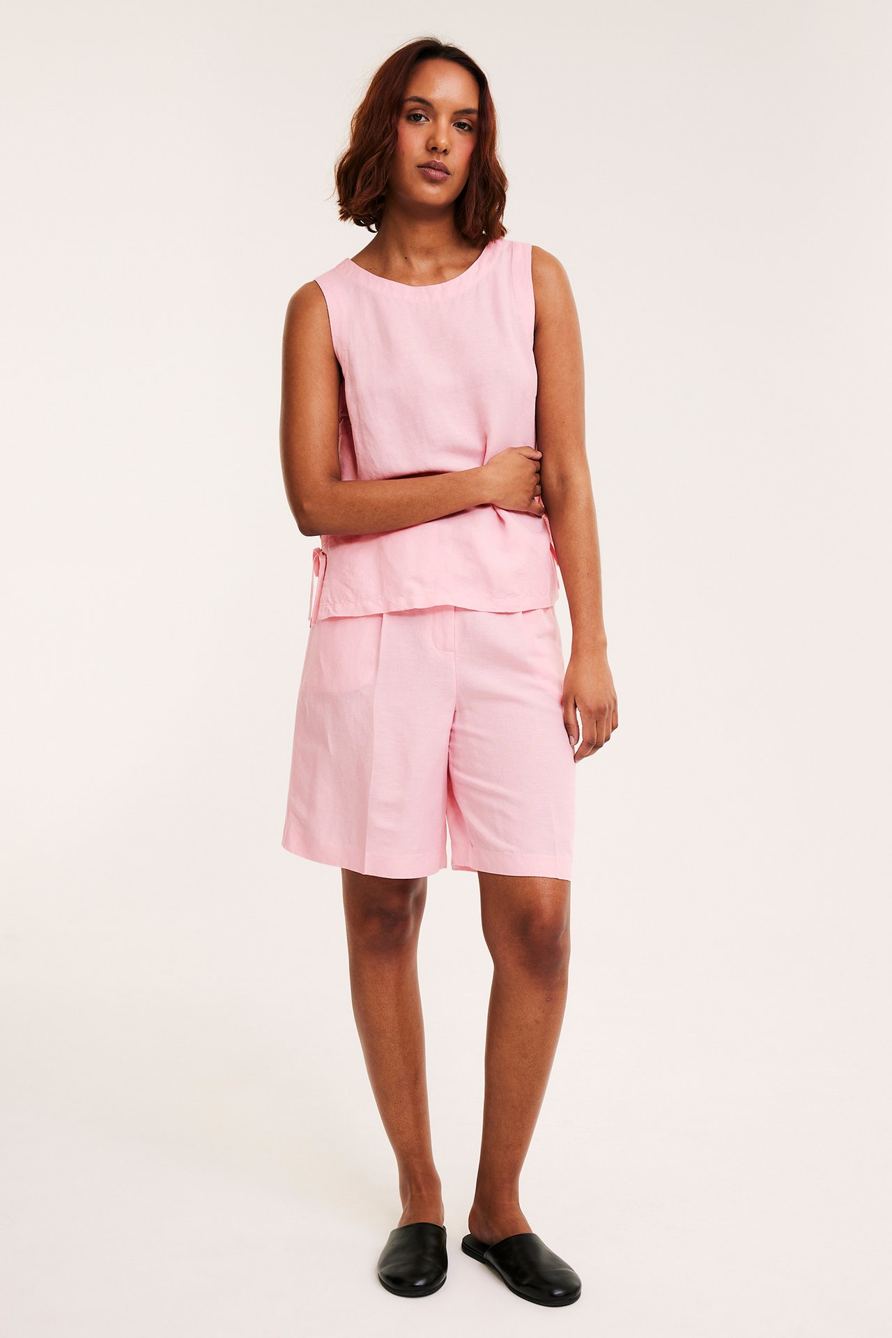Frontbilde av en kvinne i rosa linblanding-shorts, en matchende rosa ermeløs topp og sorte tøfler.