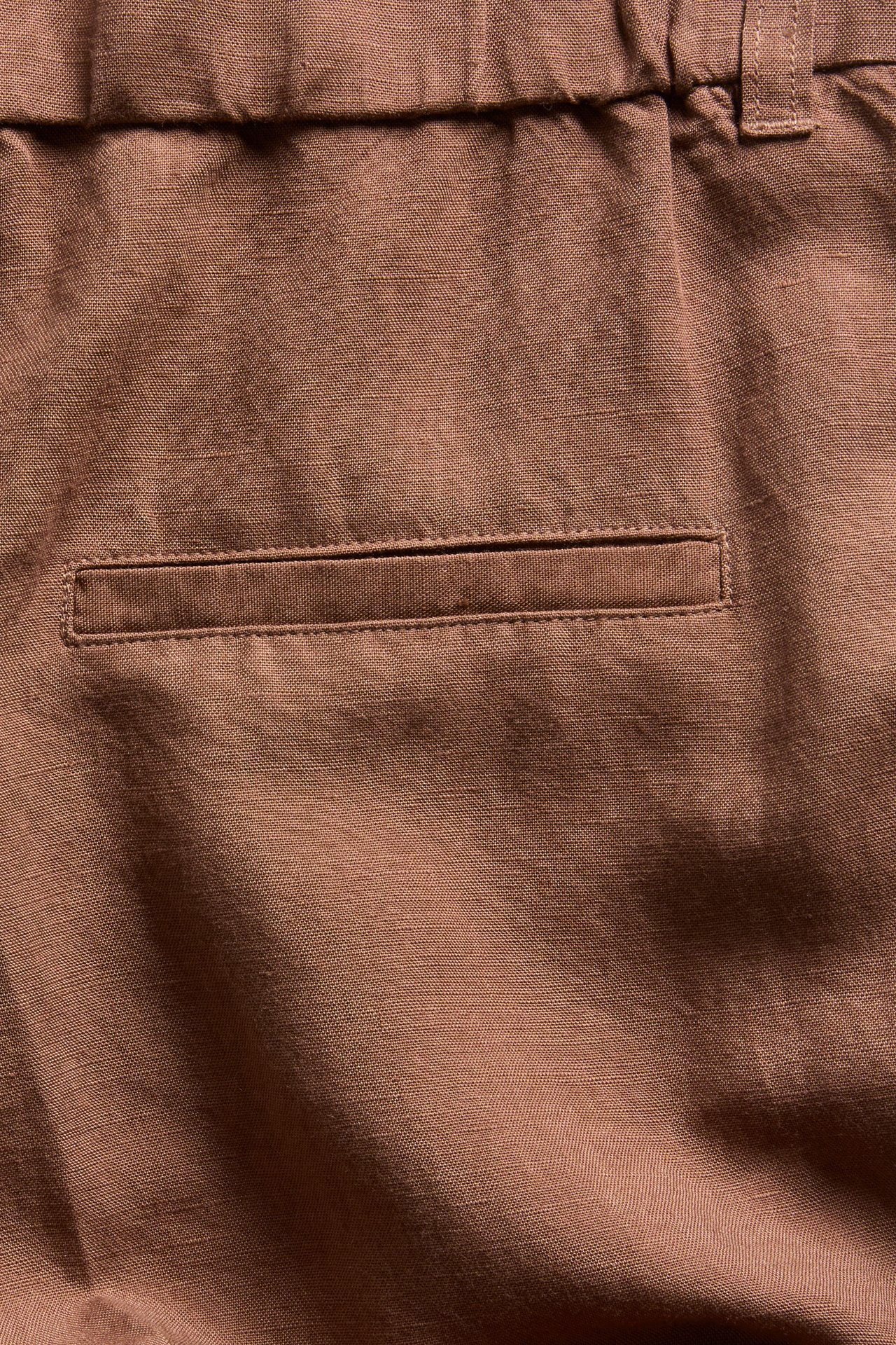 Nærbilde bakfra av brune lin-miks-shorts med elastisk midje og en passpolert lomme.