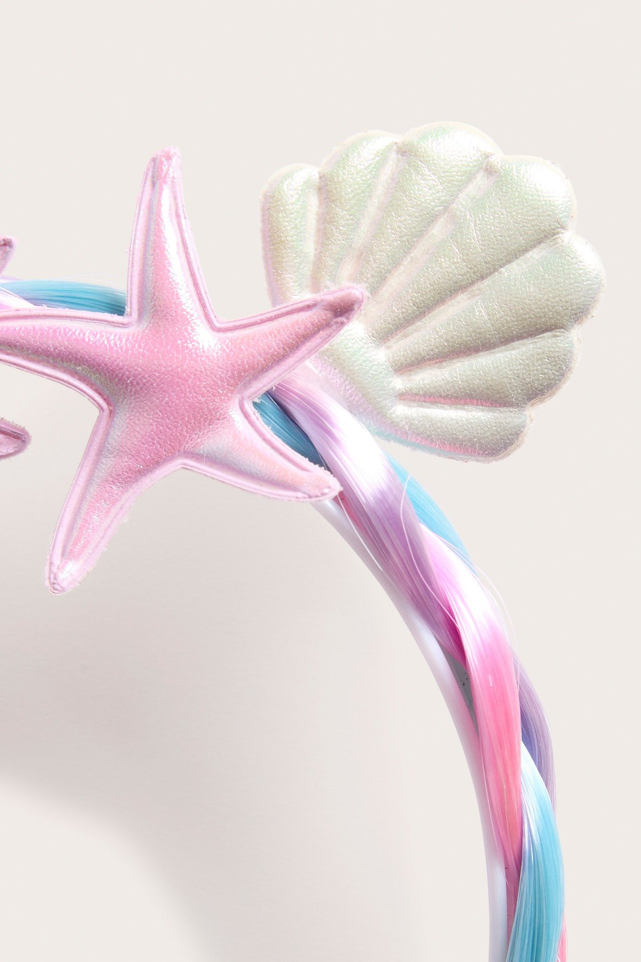 Lähikuva päänauhasta punottuine pinkkeine, sinisine, violetteine tekohiuksineen, pinkki meritähti, helmiäiskuori.