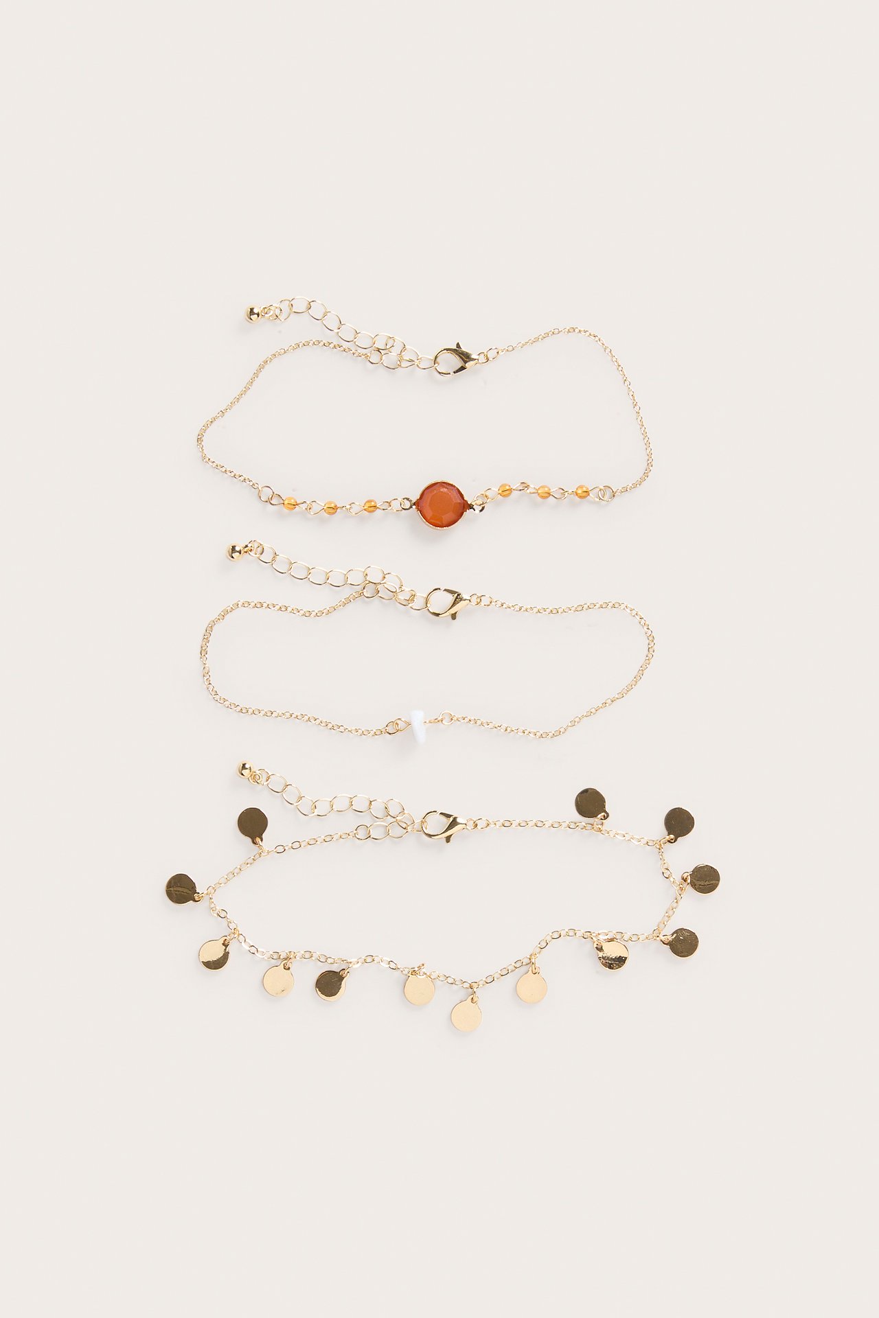 Nærbilde av tre gullfargede ankelkjeder med karabinkroker, med steiner, perler og skiver.