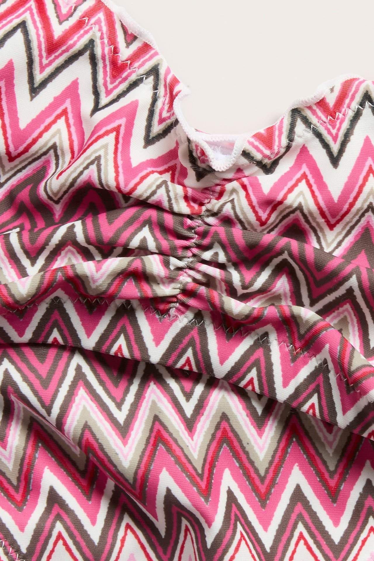 Närbild av en rosa, vit, brun och röd sicksackmönstrad bikinitopp med rynk framtill.