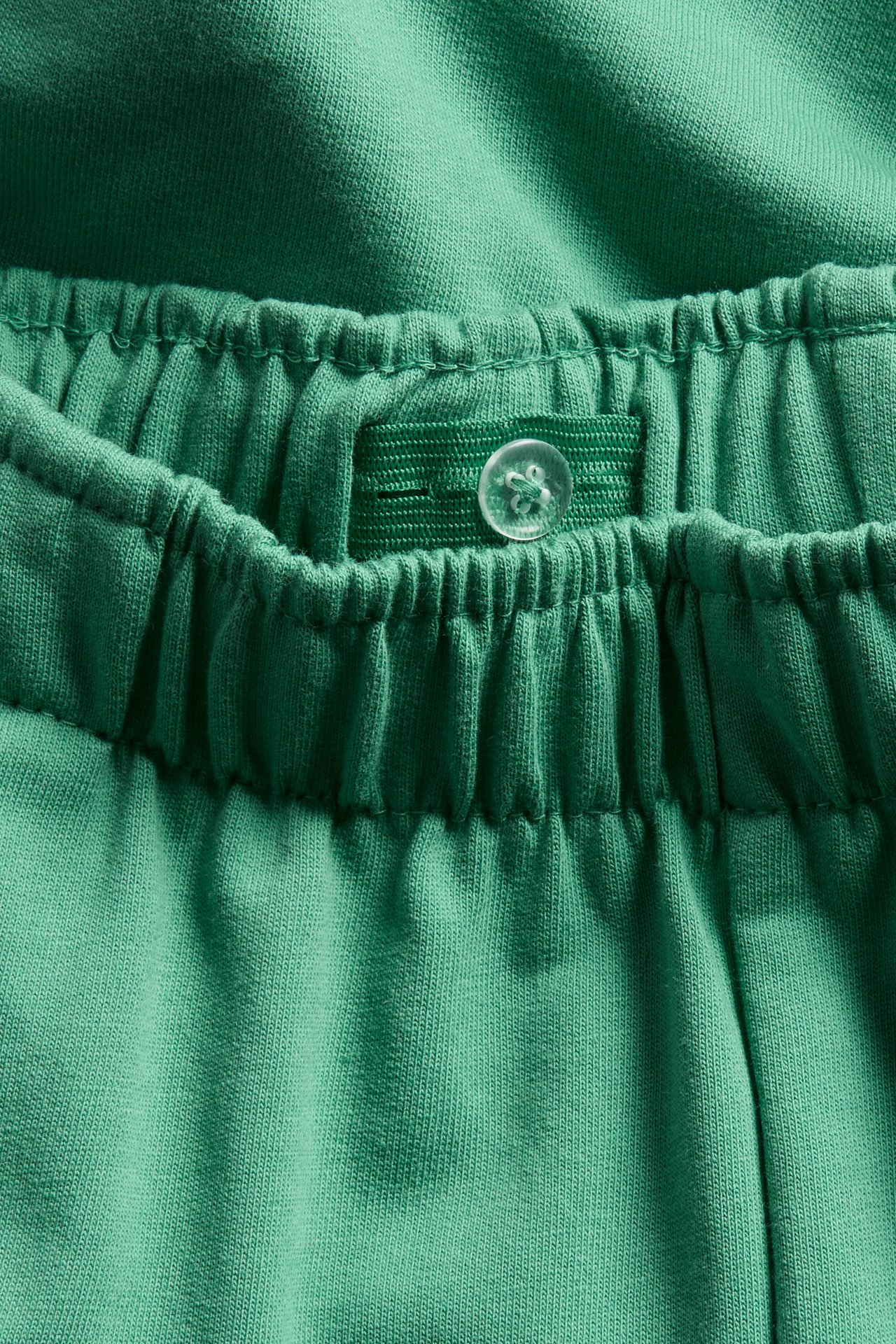 Lähikuva vihreistä trikooshortseista, joissa resori vyötäröllä ja sisäinen nappisäätö.