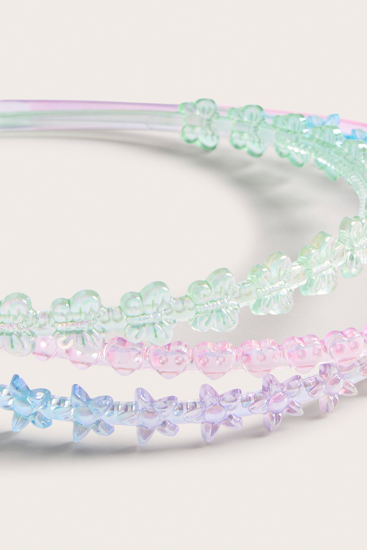 Lähikuva: Kolme irisoivaa muovipantaa vihreillä perhosilla, pinkeillä sydämillä ja sinisillä tähdillä.