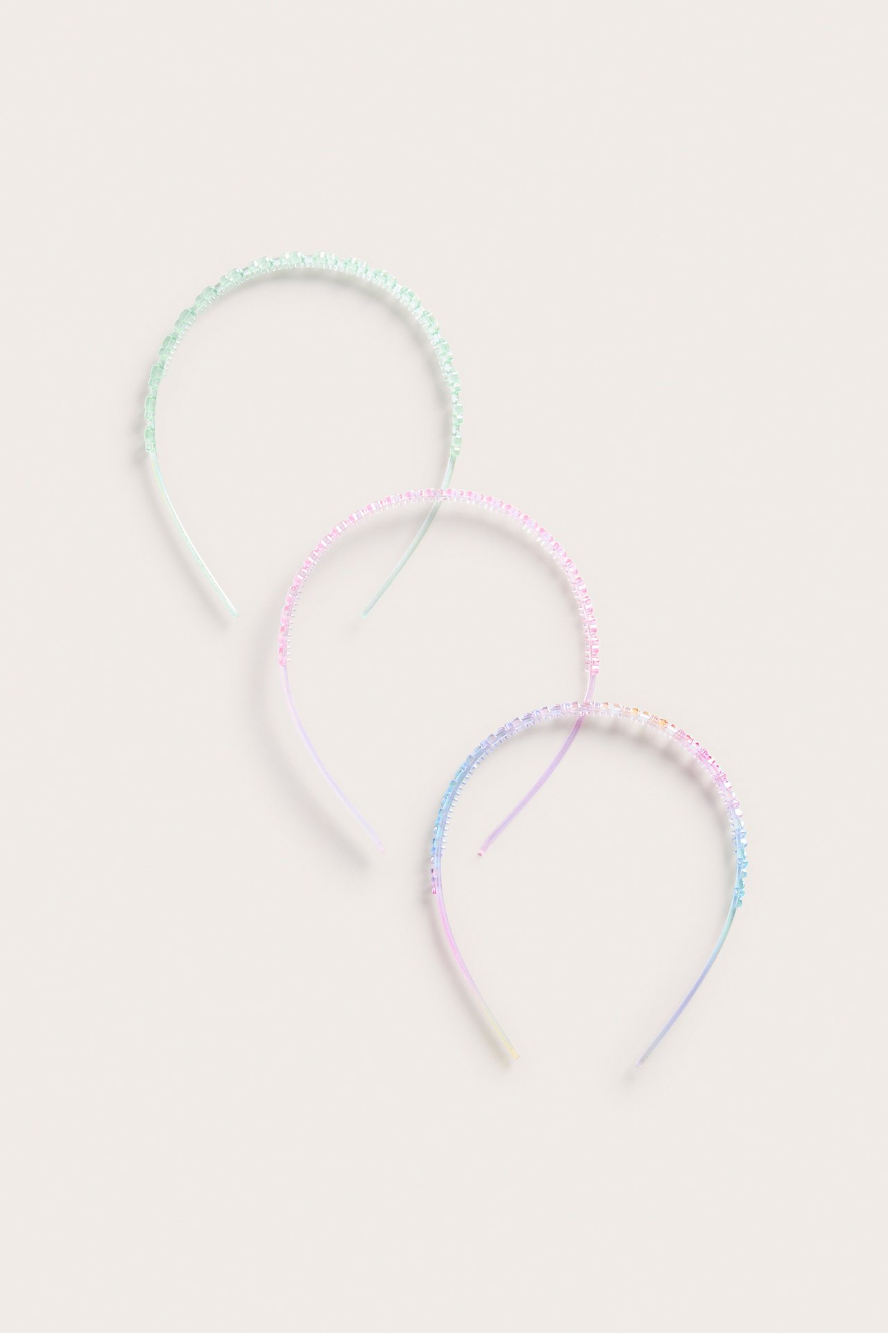 Ylhäältä kuvattu kolme muovista hiuspantaa: vaaleanvihreä, vaaleanpunainen ja sininen, sateenkaari-glitterkuviolla.