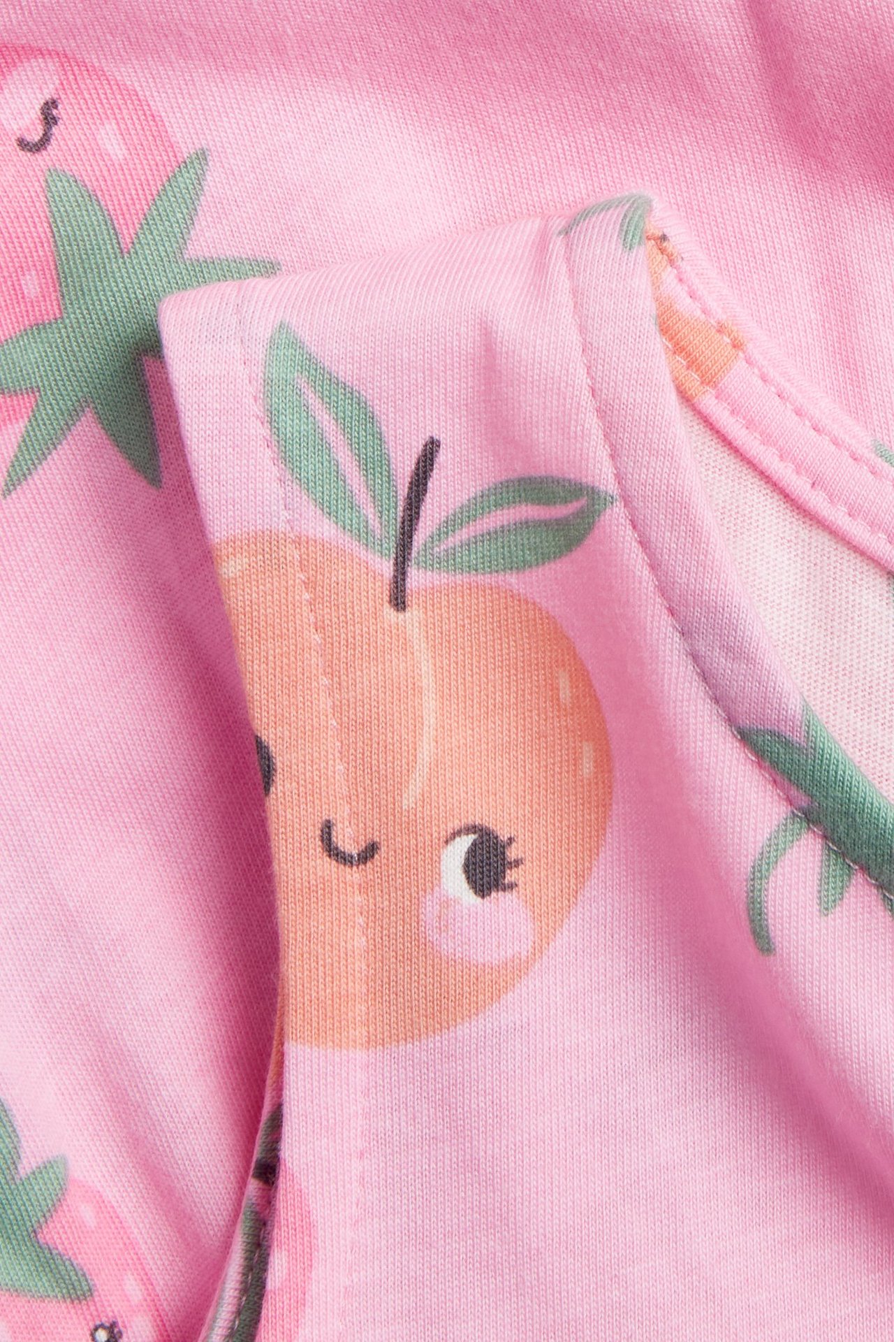 Zbliżenie jasnoróżowego bawełnianego dżerseju sukienki z wzorem brzoskwiń i truskawek.