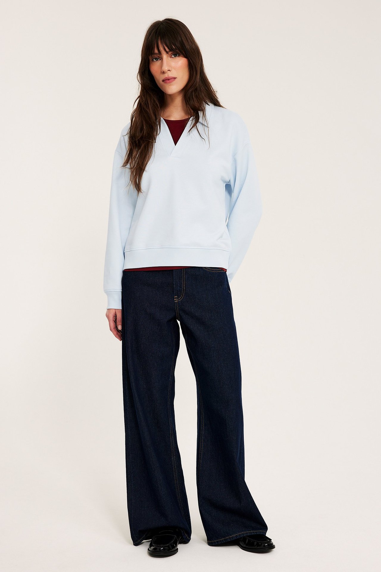 Edestäpäin: nainen vaaleansinisessä V-aukkoisessa collegepaidassa, tummanpunaisen topin ja tummansinisten leveälahkeisten farkkujen kanssa.