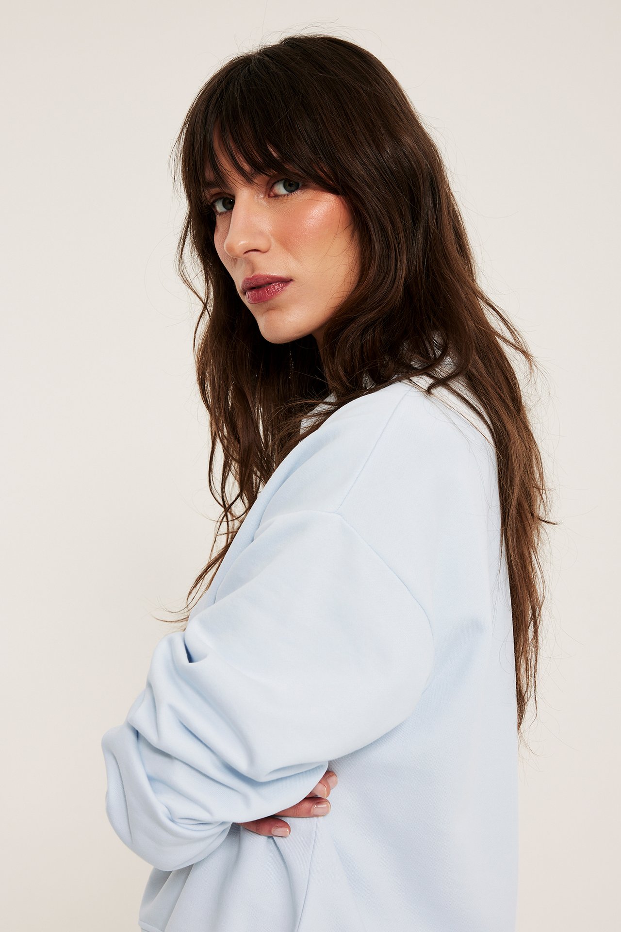 Sivusuunnasta kuvattu nainen yllään vaaleansininen pitkähihainen puuvillapaita kauluksella, kädet ristissä.