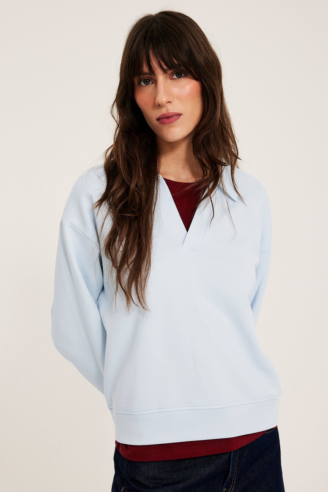 Nainen edestäpäin vaaleansinisessä puuvillacollegepaidassa, jossa on kaulus, tummanpunaisen topin päällä.