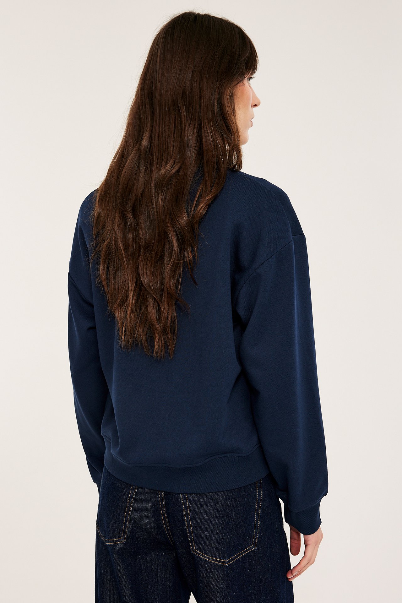 Nainen takaa/sivulta tummansinisessä puuvillapaidassa kauluksella ja tummansinisissä farkuissa.