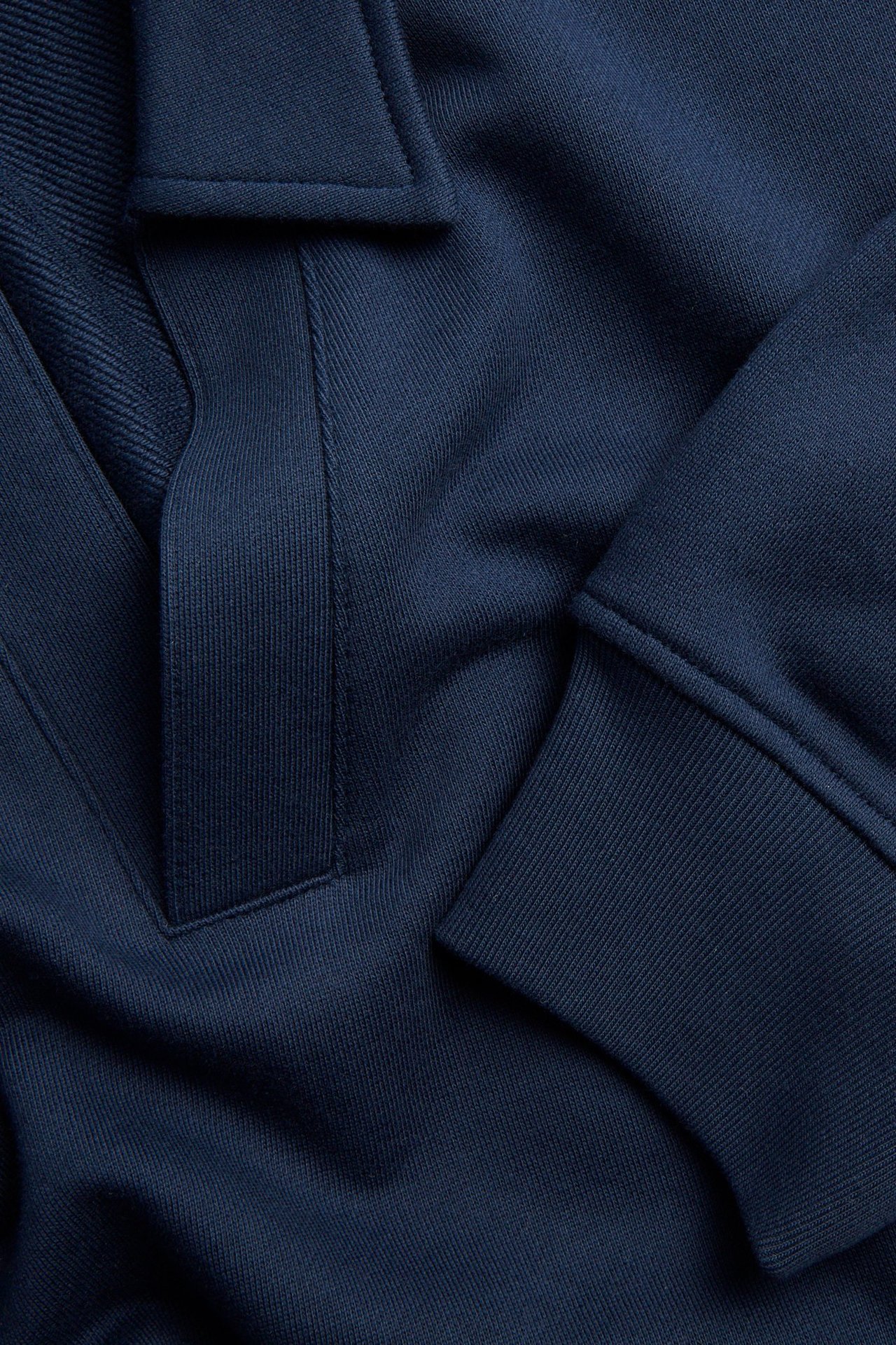 Zbliżenie na granatową bawełnianą bluzę, ukazujące dekolt w szpic z prążkowaną plisą i prążkowany mankiet.