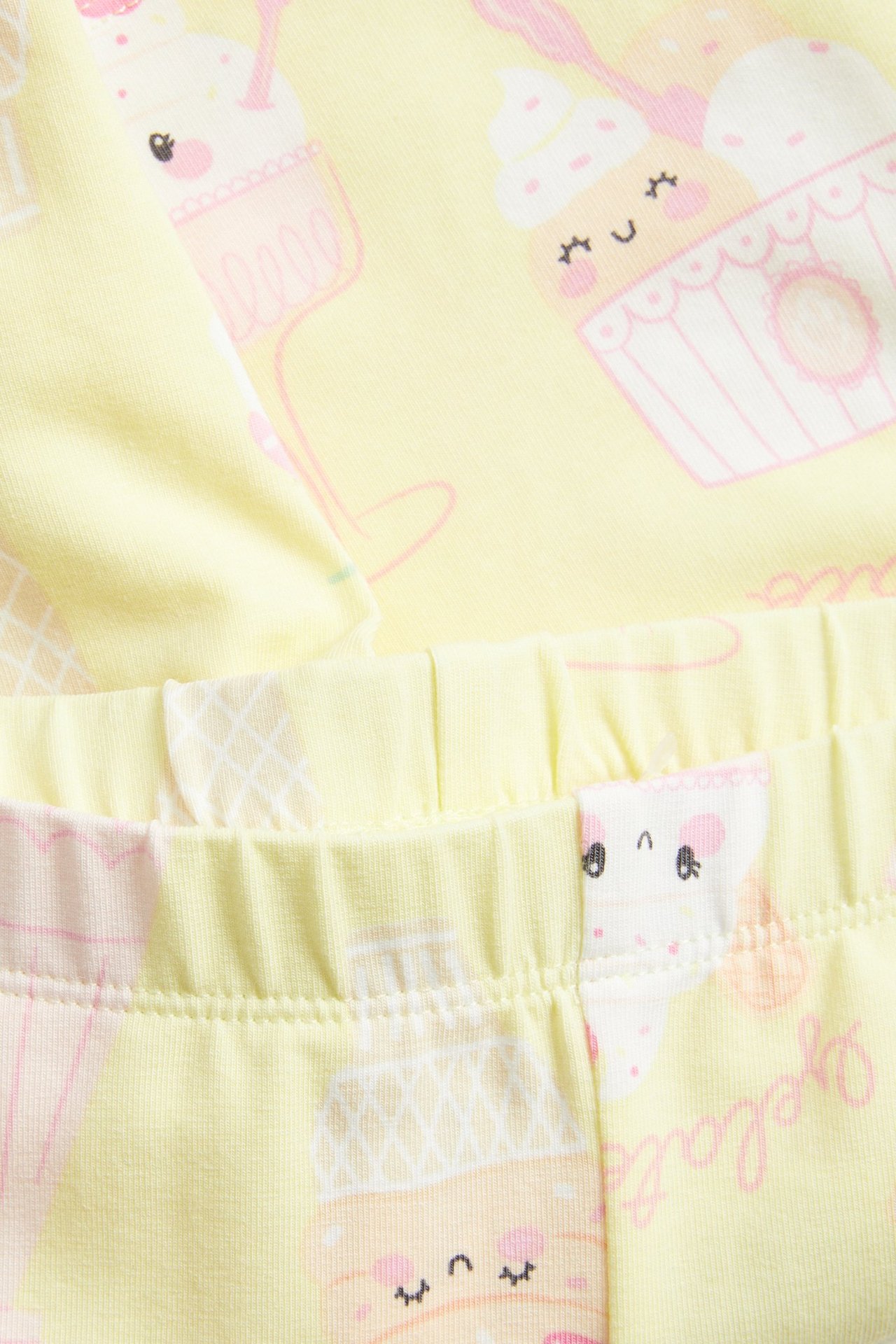 Lähikuva vaaleankeltaisista lasten pyöräilyshortseista, joissa on jäätelökuvio ja joustava vyötärö.