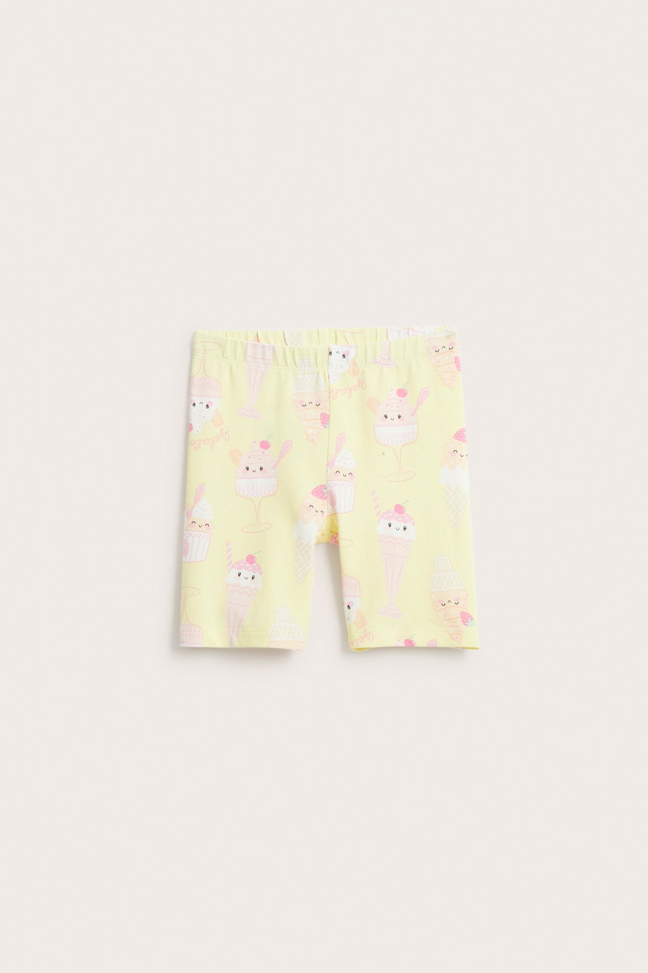 Edestä näkymä lasten vaaleankeltaisista puuvillaisista pyöräilyshortseista jäätelökuvioilla ja resori vyötäröllä.