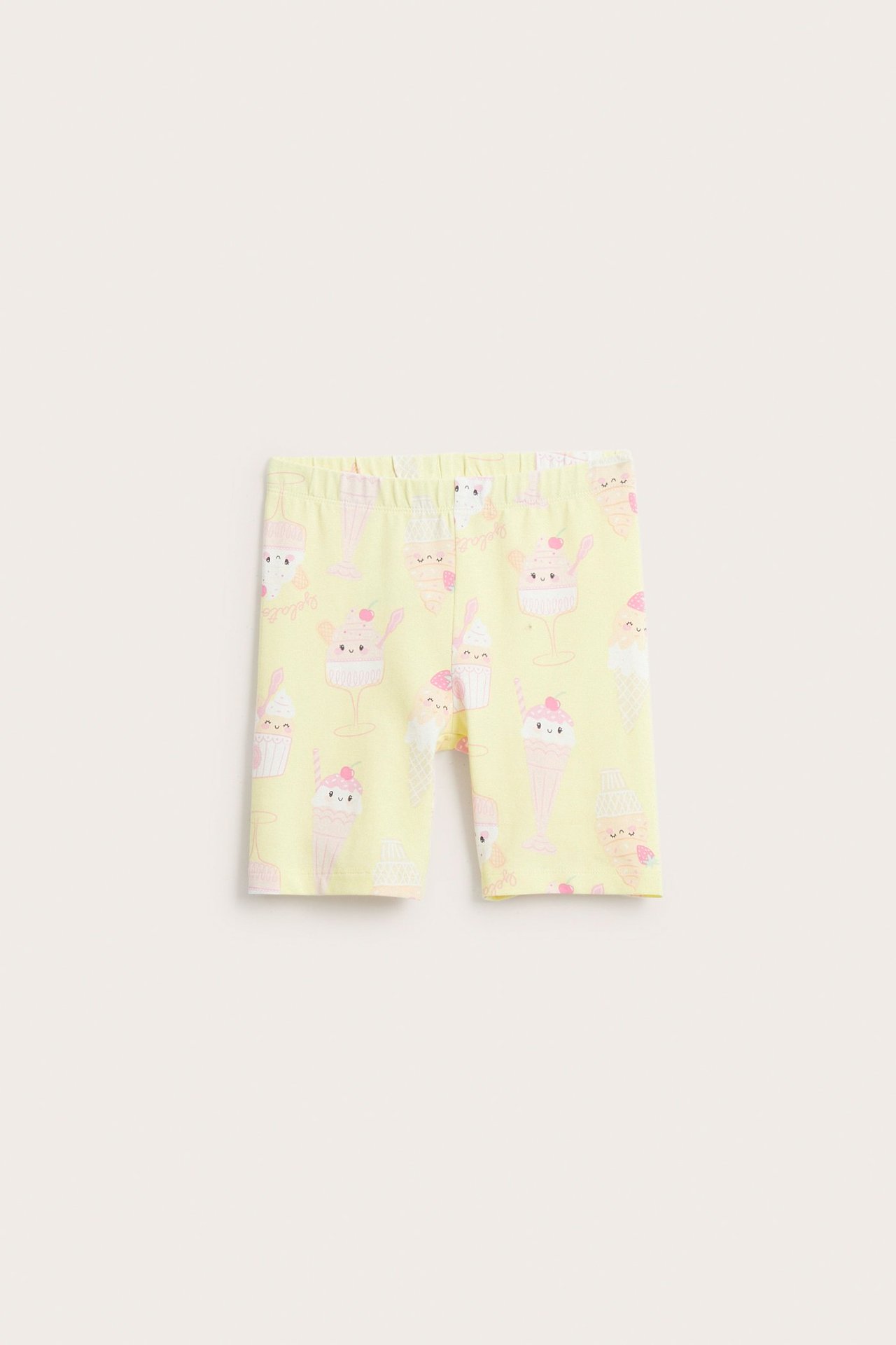 Edestä näkymä lasten vaaleankeltaisista puuvillaisista pyöräilyshortseista jäätelökuvioilla ja resori vyötäröllä.