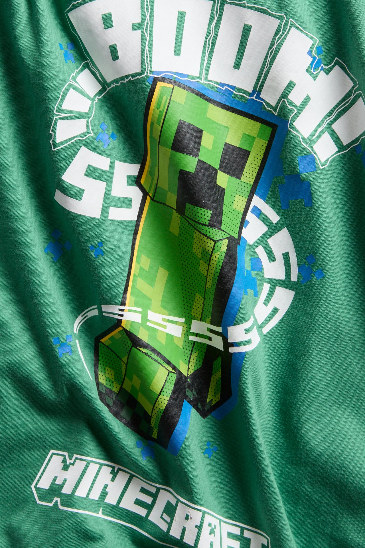 Lähikuva edestä vihreästä oversize puuvillatrikoo t-paidasta, jossa on Minecraft Creeper -printti.