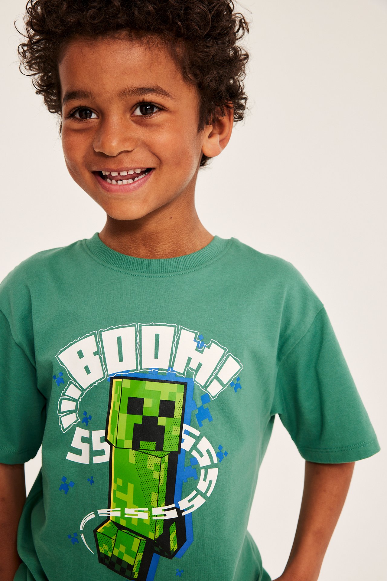 Närbild framifrån: leende barn i grön oversize t-shirt i bomull med Minecraft Creeper-tryck.