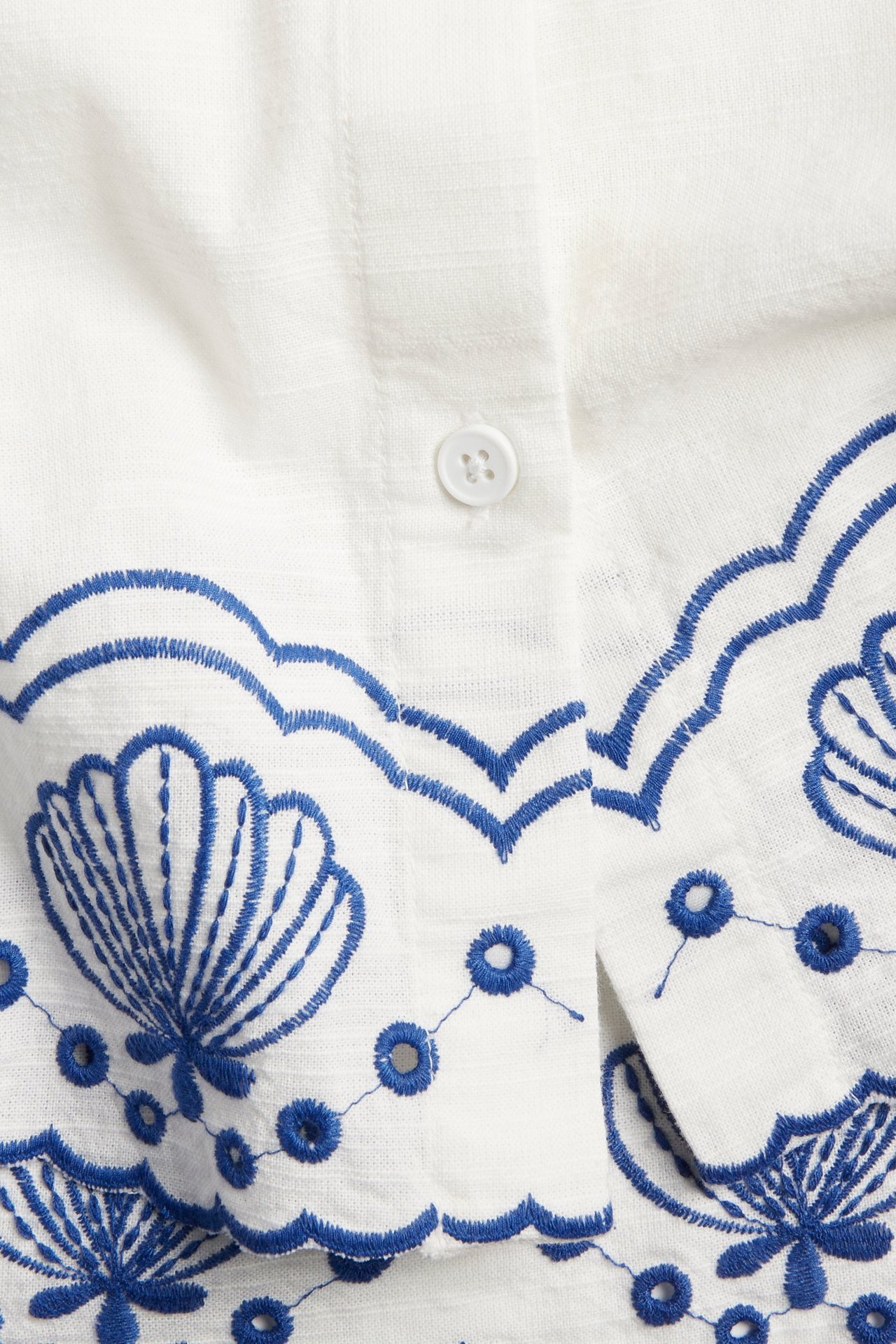 Zbliżenie białej bawełnianej koszuli z niebieskim haftem angielskim i białym guzikiem.
