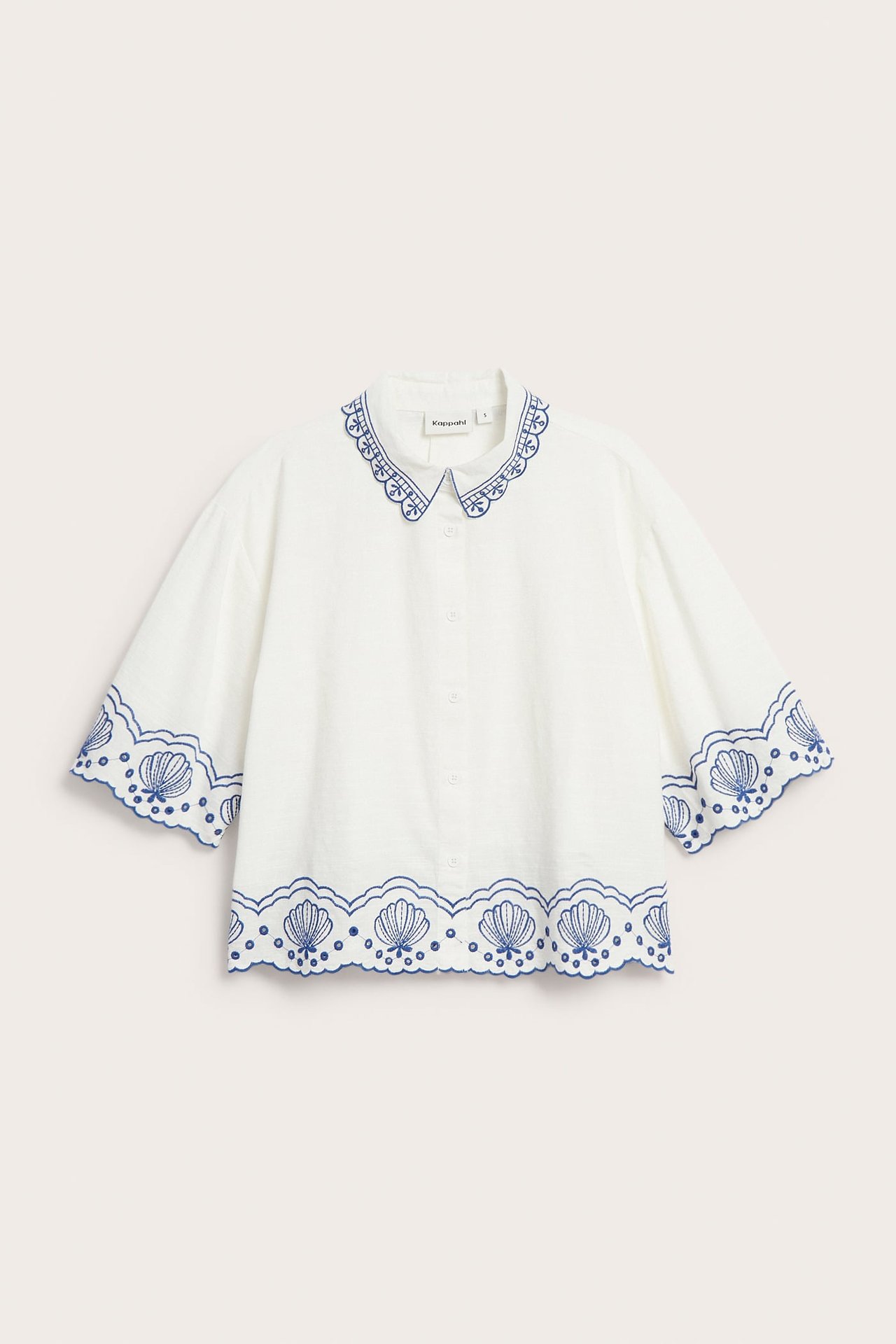 Frontvy: vit kortärmad bomullsskjorta med blå broderie anglaise på krage, ärmslut och nederkant.