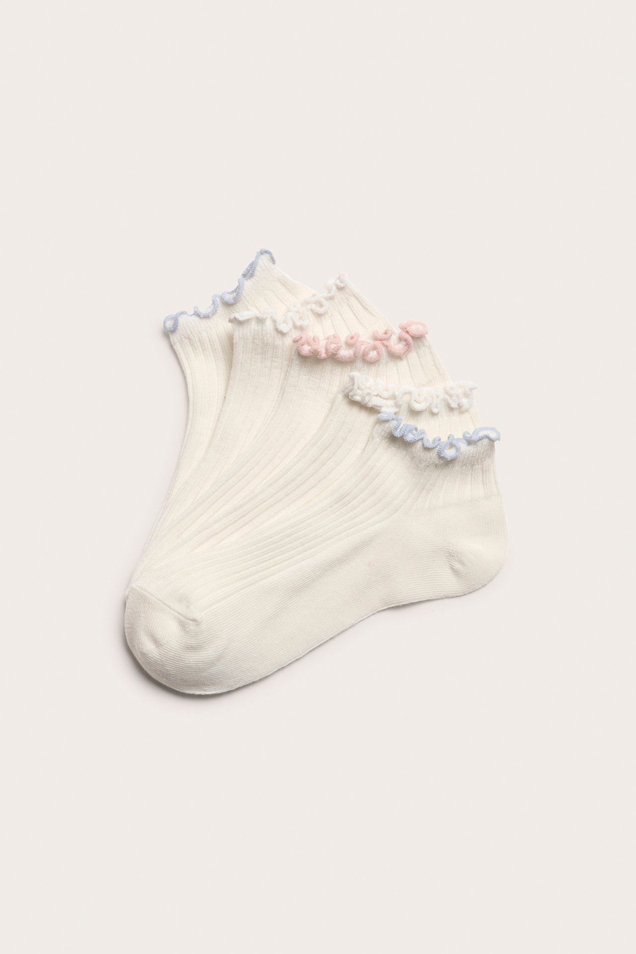 Närbild av 5-pack vita ribbade sneakersstrumpor med volangkanter i vitt, rosa och ljusblått.