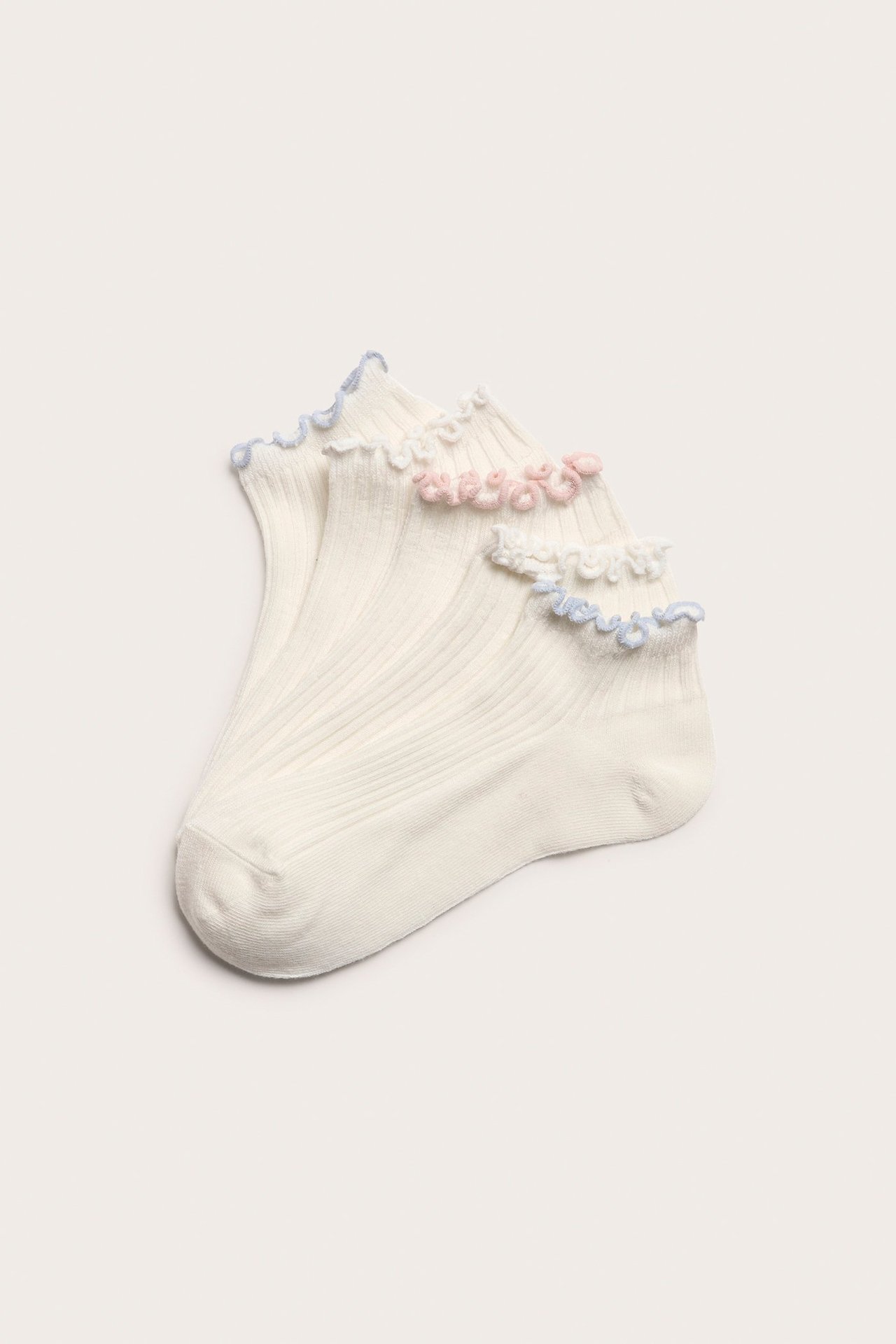 Zbliżenie na 5-pak białych, prążkowanych skarpetek sneakers z falbankami białymi, różowymi i jasnoniebieskimi.