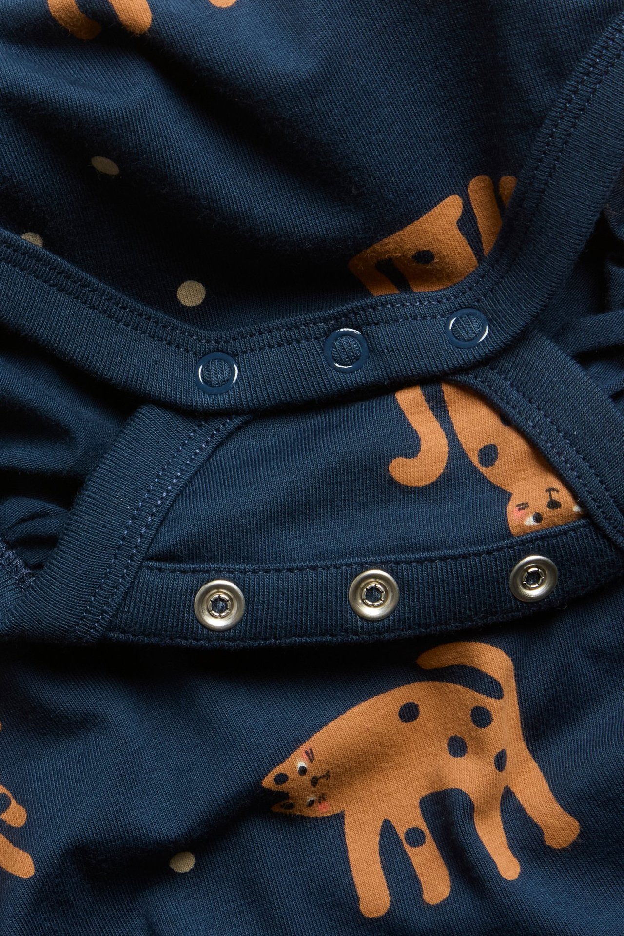 Nærbilde av en mørkblå ribbet babybody med brunt dyremønster og synlige trykknapper.