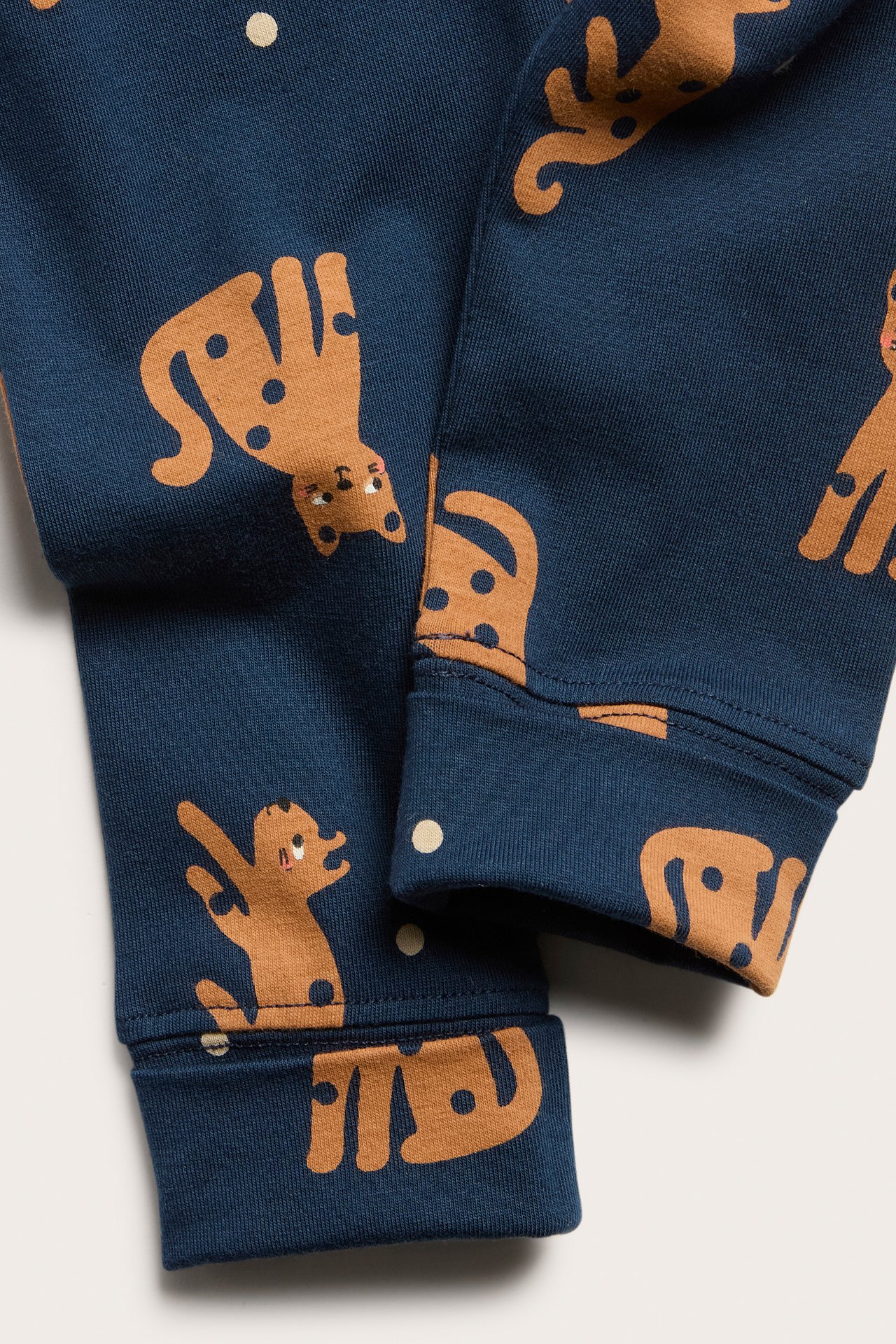 Nærbilde av mørkeblå ribbestrikkede baby-leggings med brunt dyremønster og lyse prikker, med nedbrettbare mansjetter.