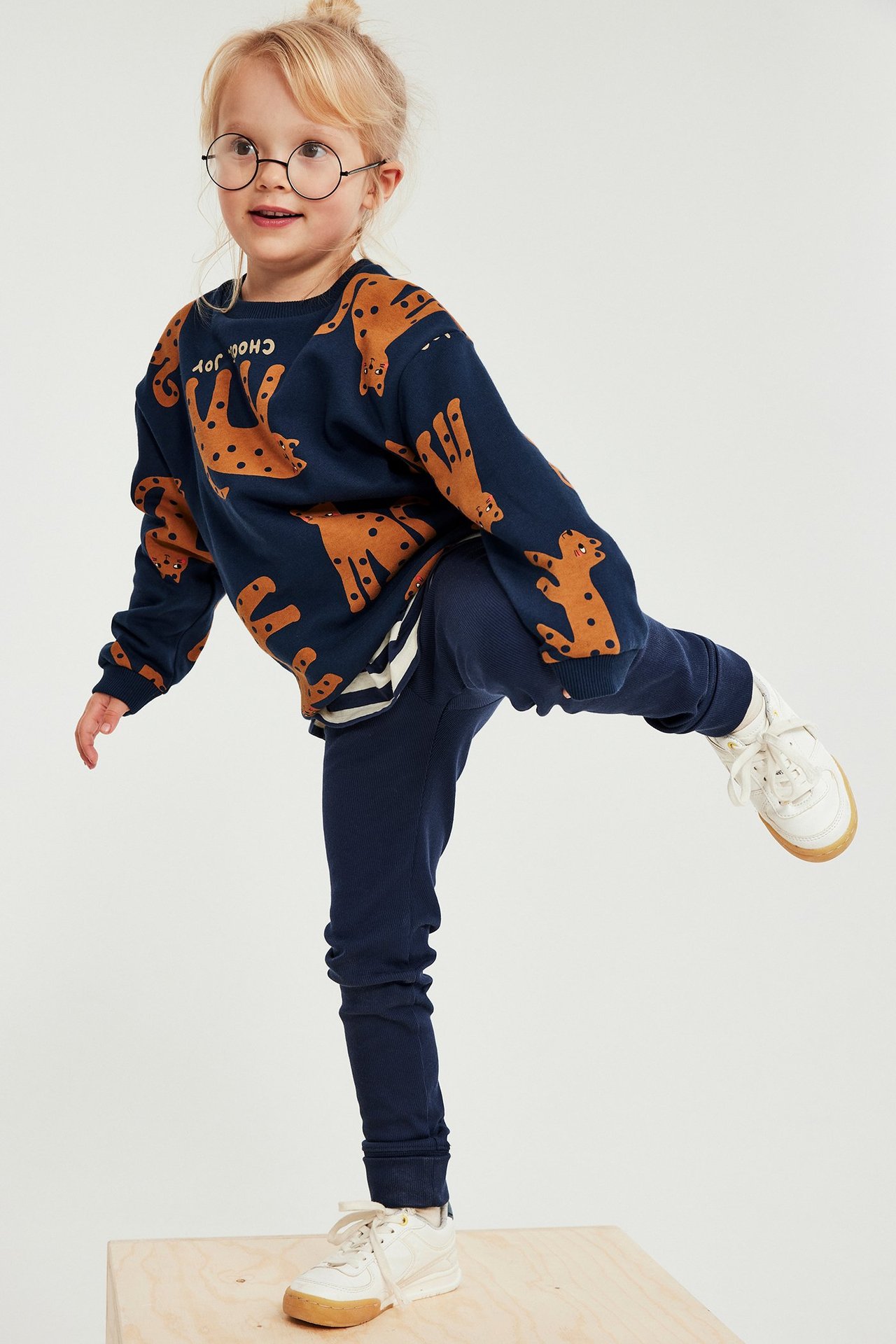 Forfra: et barn i en mørkeblå mønstret genser, mørkeblå leggings og hvite sneakers.