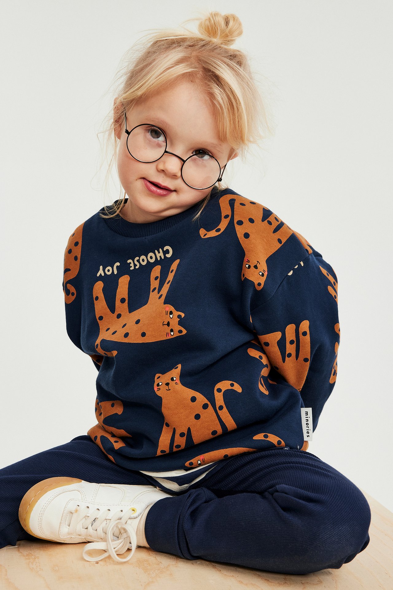 Widok z przodu: dziecko w granatowej wzorzystej bluzie, granatowych spodniach i białych tenisówkach.