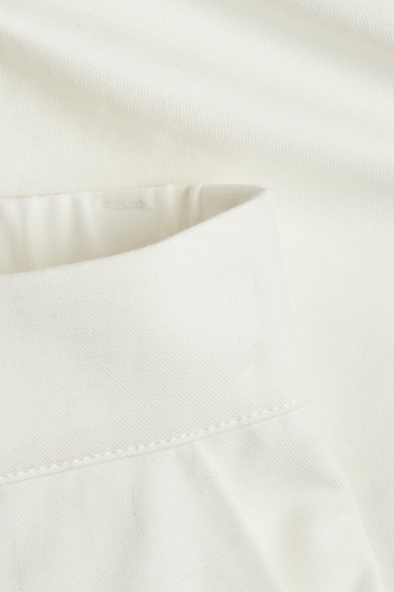 Lähikuva valkoisista puuvilla-pellava Bermudahortseista, näyttäen kankaan ja vyötärön ompeleet.