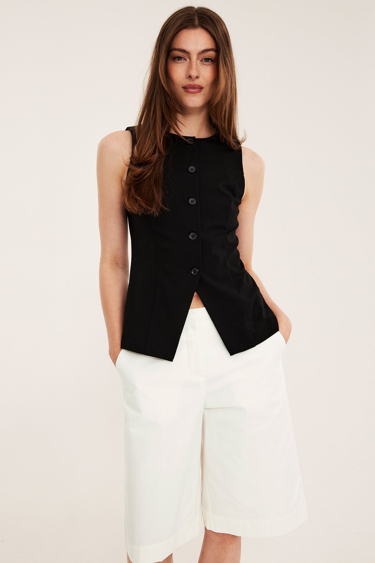 Forfra, kvinne i hvite knelange bermudashorts og en svart ermeløs knappetopp.