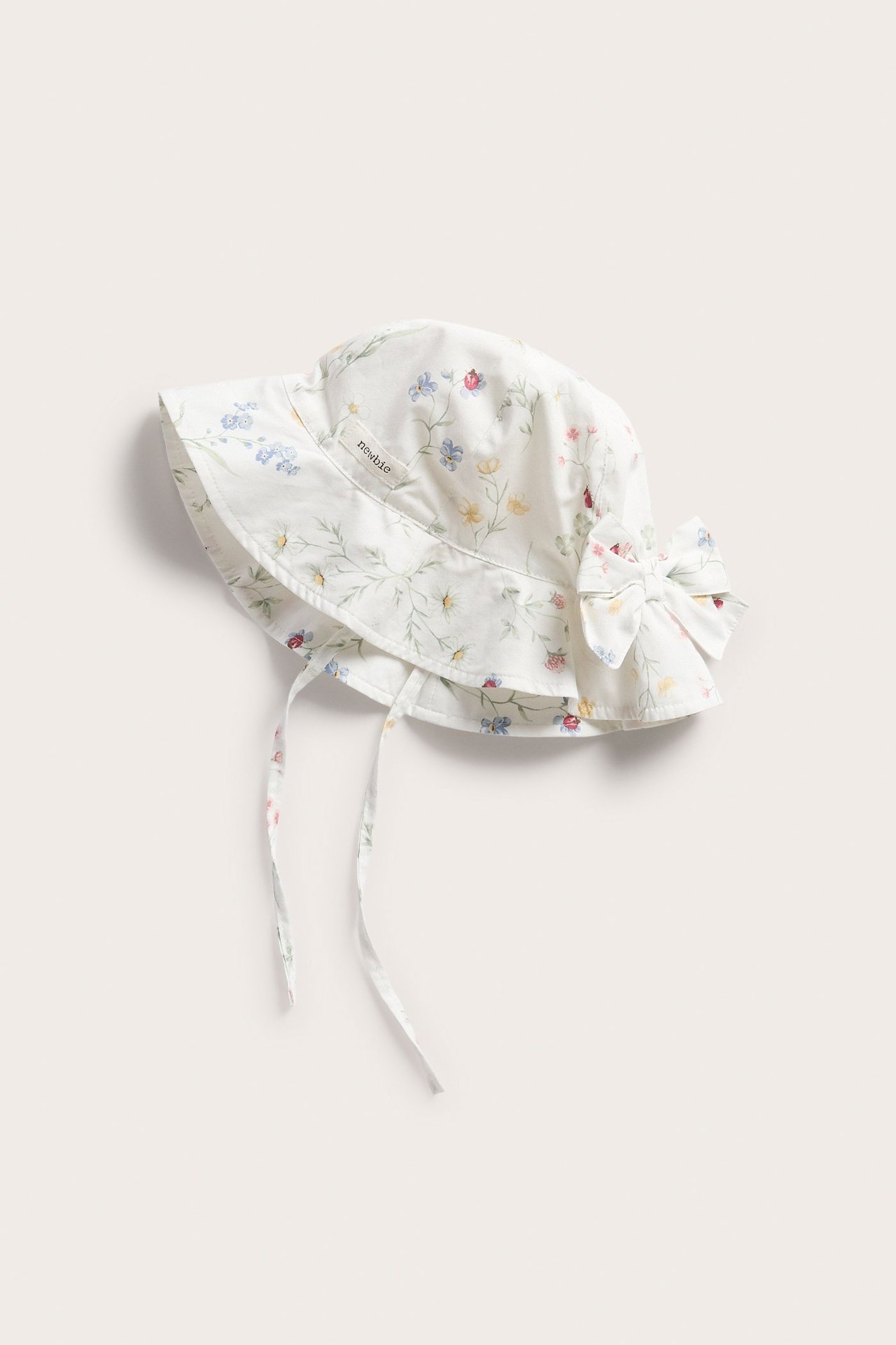 Widok z przodu: kremowy, kwiecisty kapelusz przeciwsłoneczny dla niemowląt z kokardką i wiązaniami.