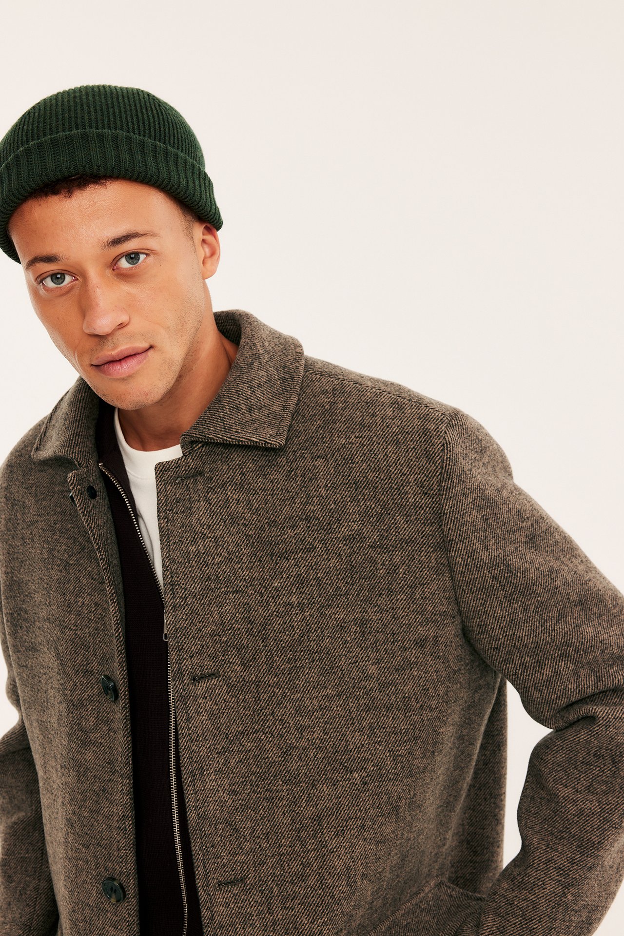 Front view, mann med brun tweedjakke, mørkbrun cardigan, hvit t-skjorte og grønn lue.