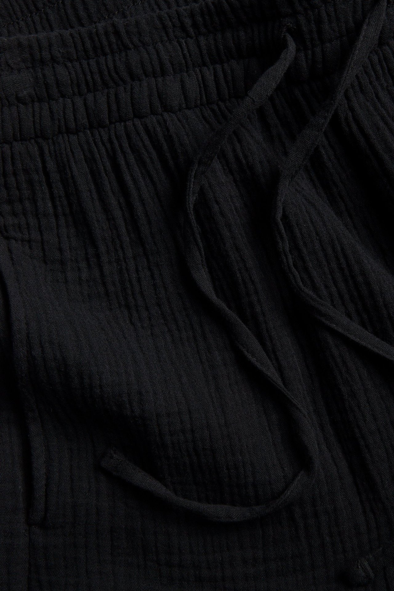 Lähikuva mustista kaksoismysliinishortseista joustovyötäröllä ja kiristysnyörillä.