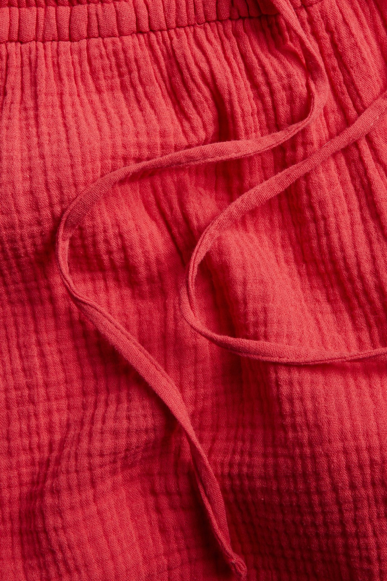Närbild av röda strukturerade bomullsshorts med elastisk dragsko i midjan.