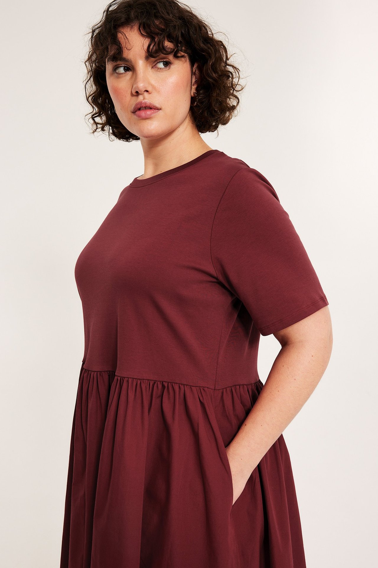 Widok z przodu: kobieta w ciemnoczerwonej sukience z krótkim rękawem, dżersejową górą, spódnicą z popeliny.