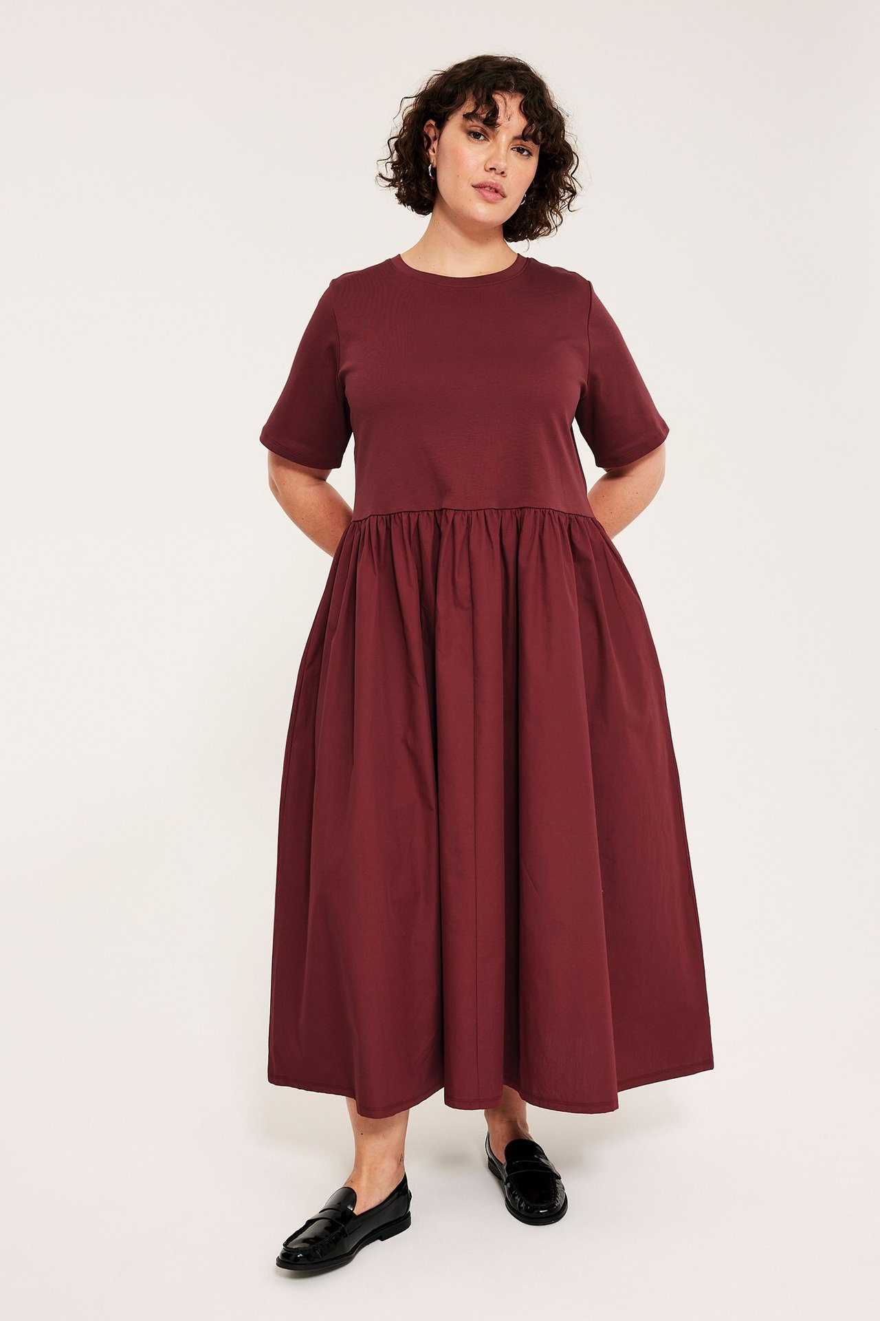 Widok z przodu: kobieta w jednolitej czerwonej sukience midi z krótkim rękawem i czarnymi mokasynami.